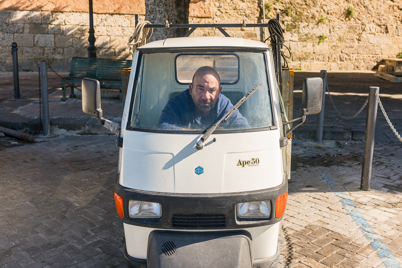 A driver inside a white three-wheeled Ape vehicle in Syracuse, Italy. Photograph by Alex Galmeanu.