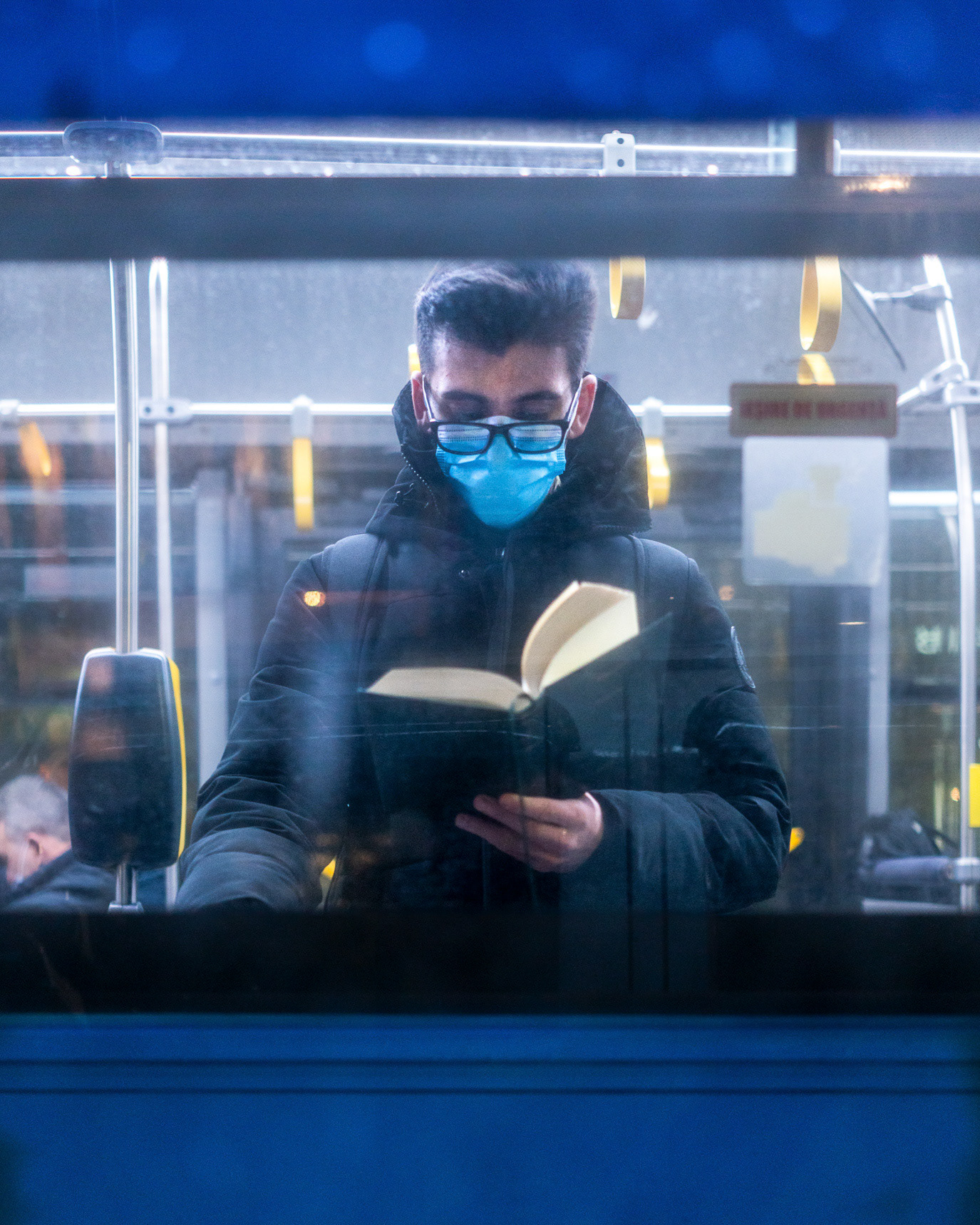 A masked passenger reading behind the blue window of a bus in Bucharest, Romania. Photograph by Alex Galmeanu.