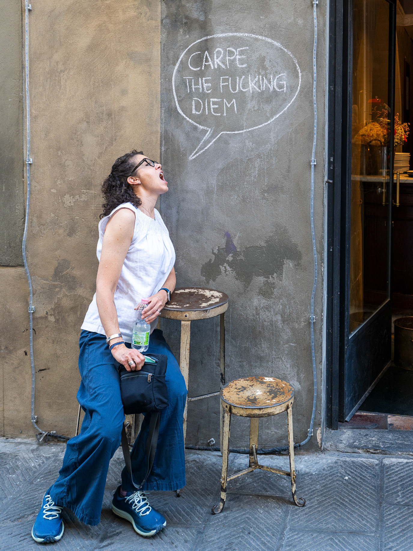 A woman leaning beneath a handwritten “Carpe diem” message in Florence, Italy. Photograph by Alex Galmeanu.