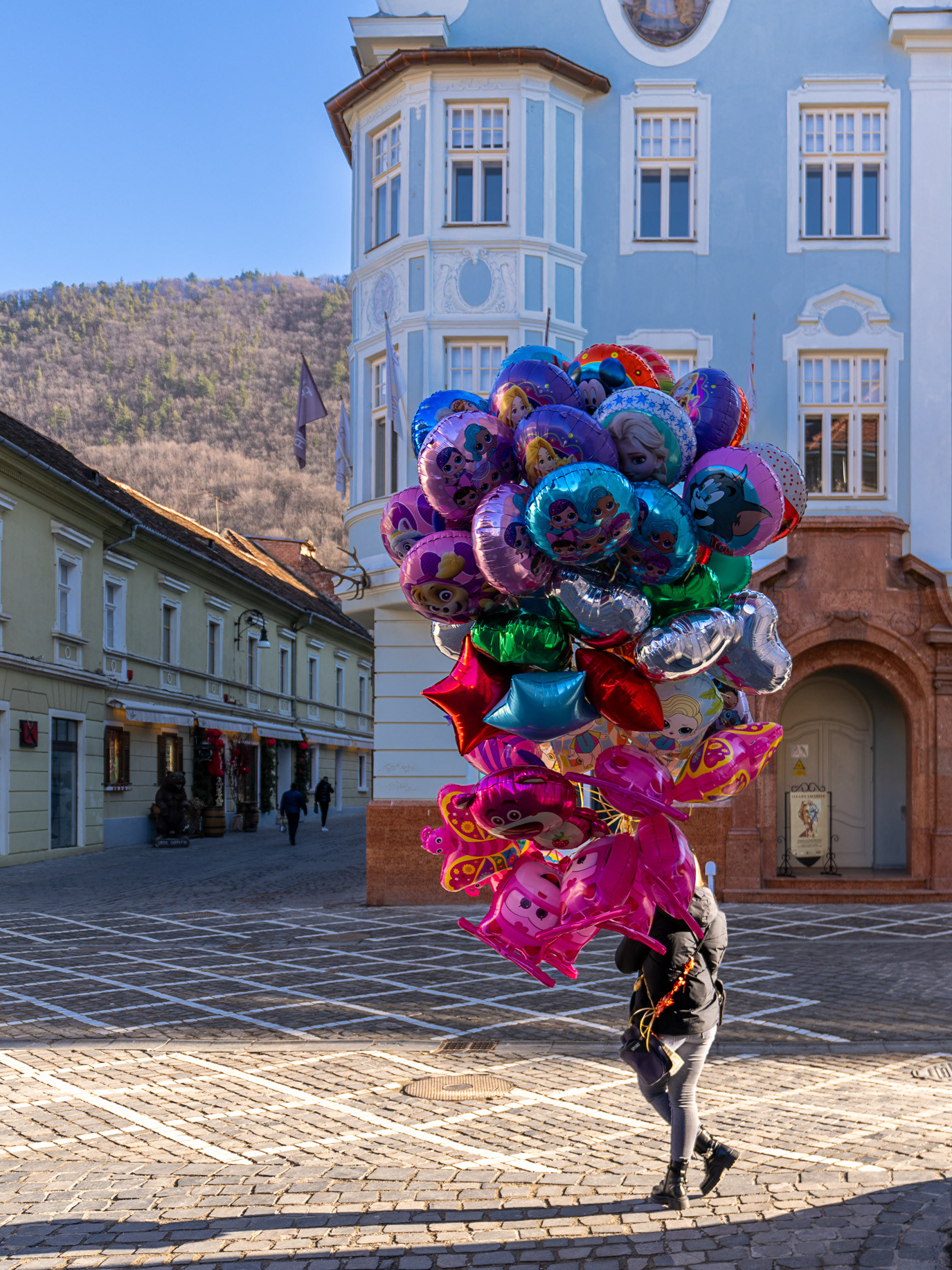 A balloon vendor almost hidden beneath a cluster of colorful balloons in Brașov, Romania. Photograph by Alex Galmeanu.