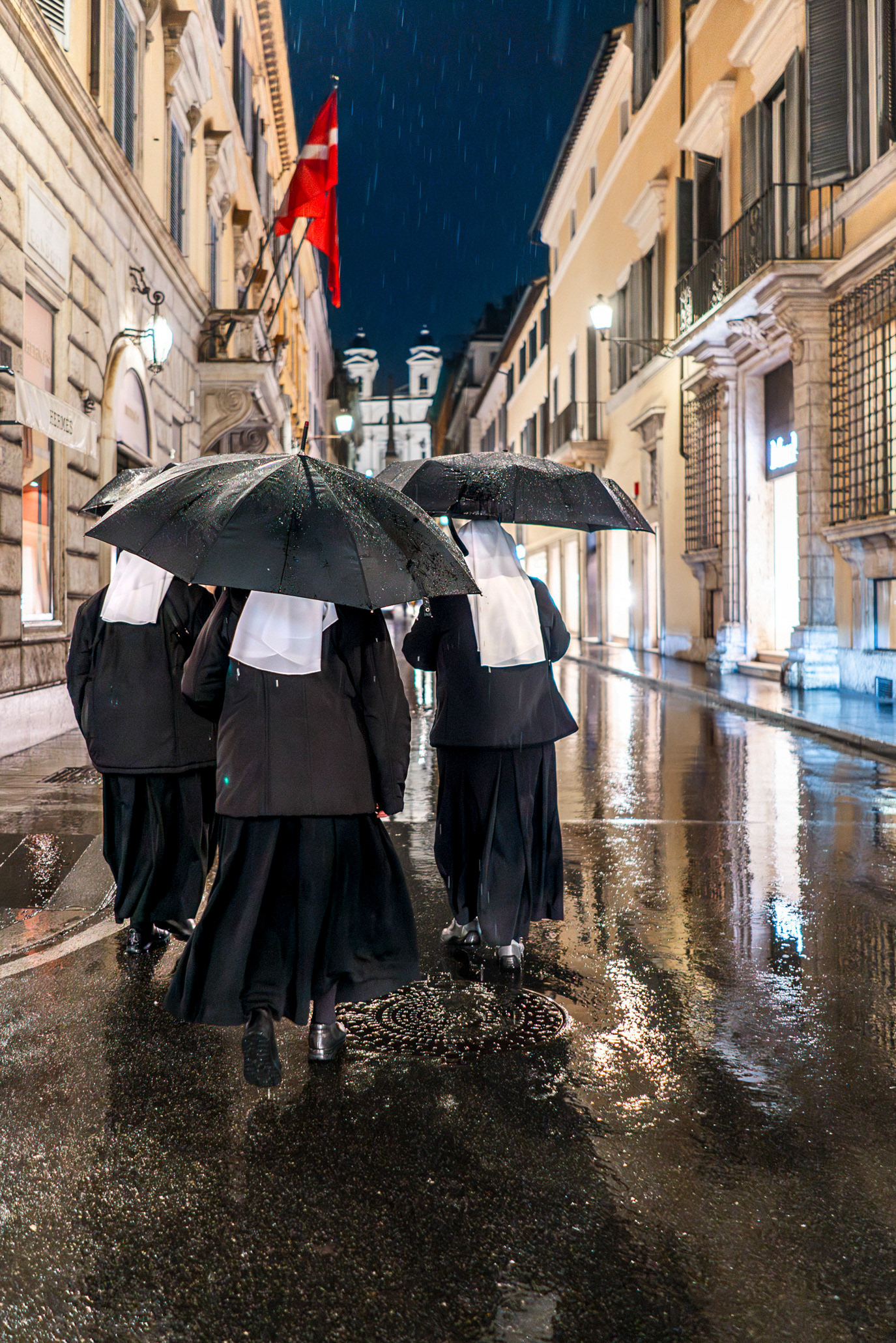 A cluster of black umbrellas moving through a rain-soaked street in Rome, Italy. Photograph by Alex Galmeanu.