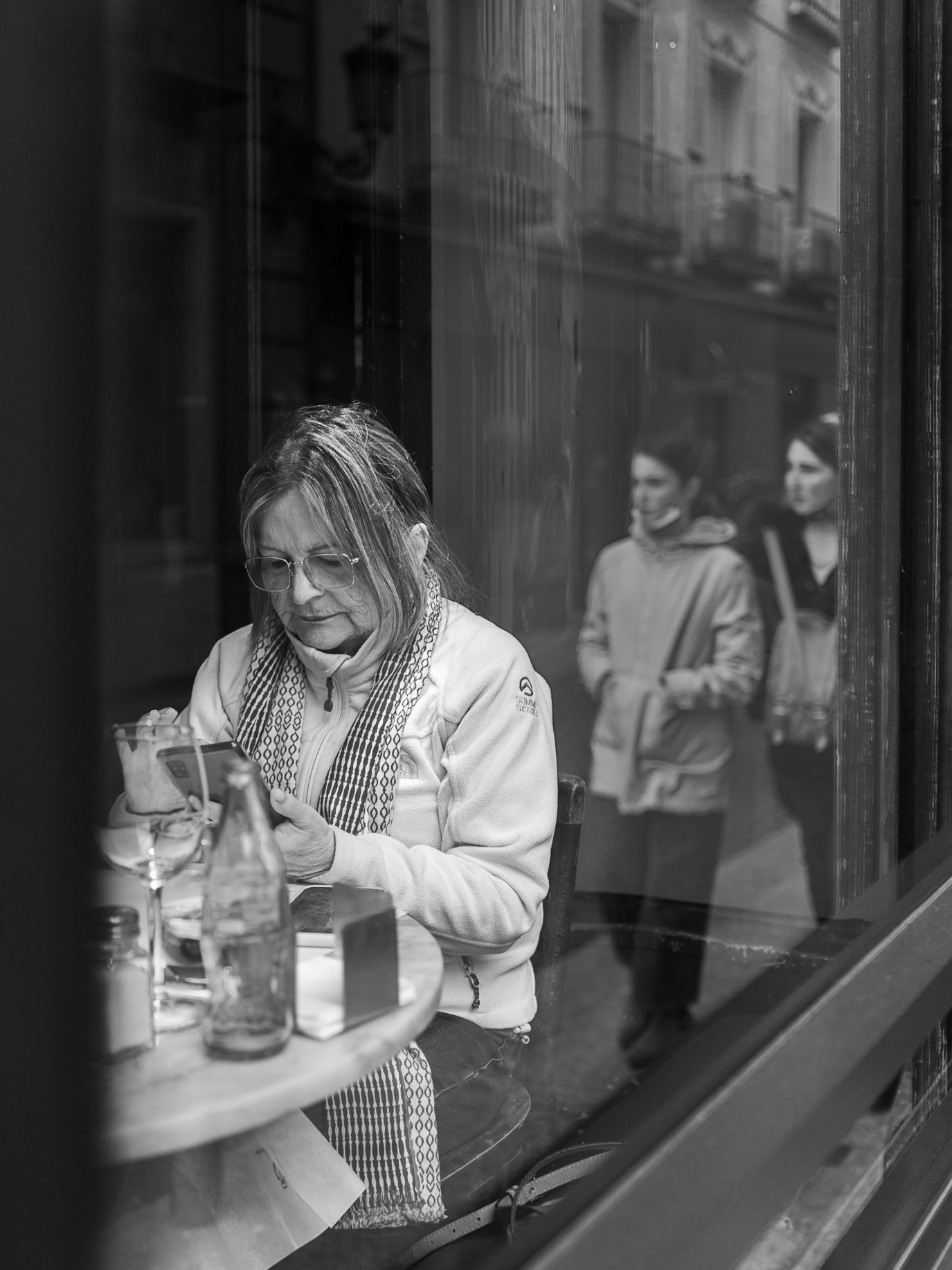 A woman at a café table seen through layered window reflections in Madrid, Spain. Photograph by Alex Galmeanu.