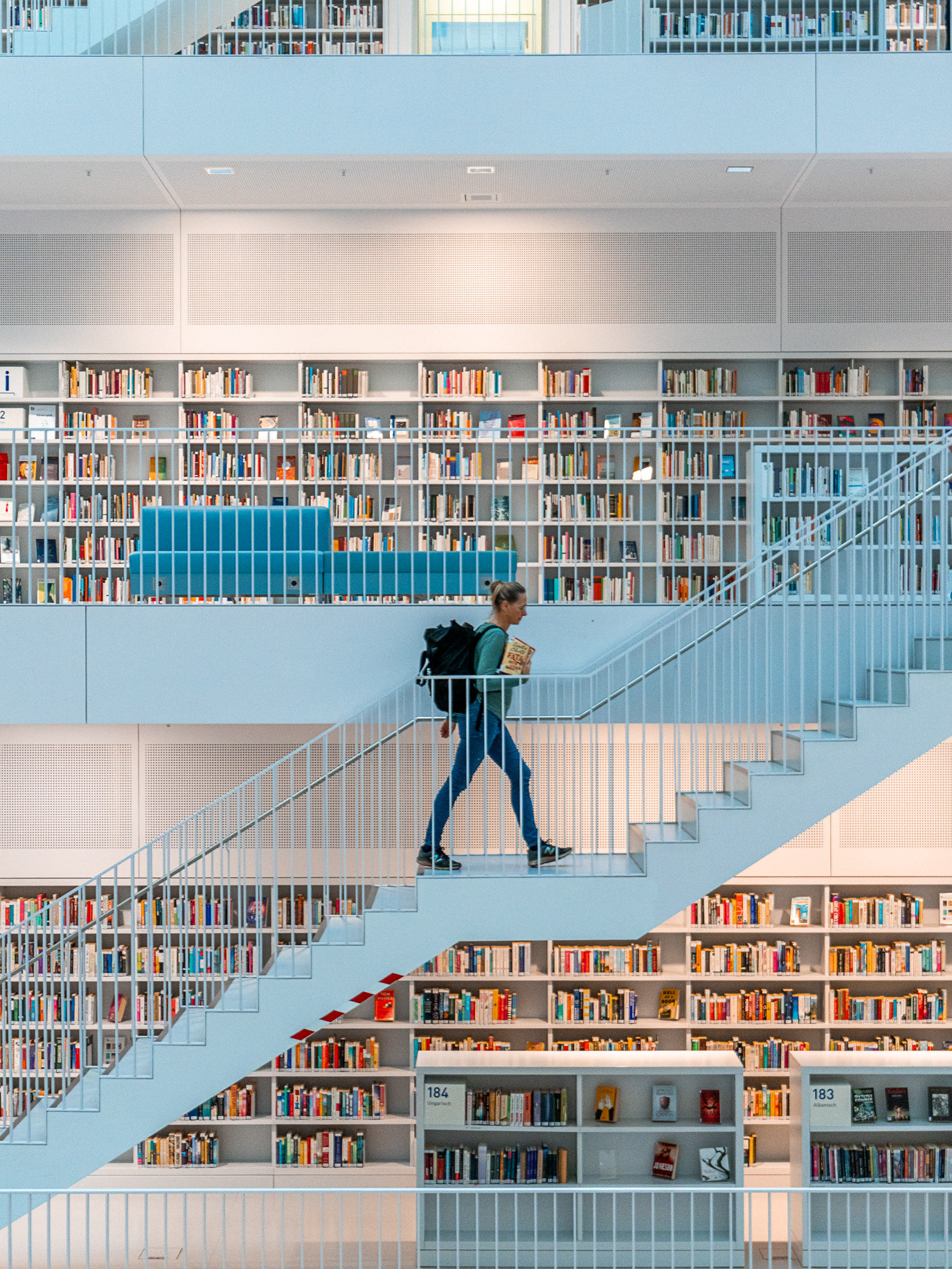 A reader carrying books along a diagonal staircase inside Stuttgart City Library, Germany. Photograph by Alex Galmeanu.