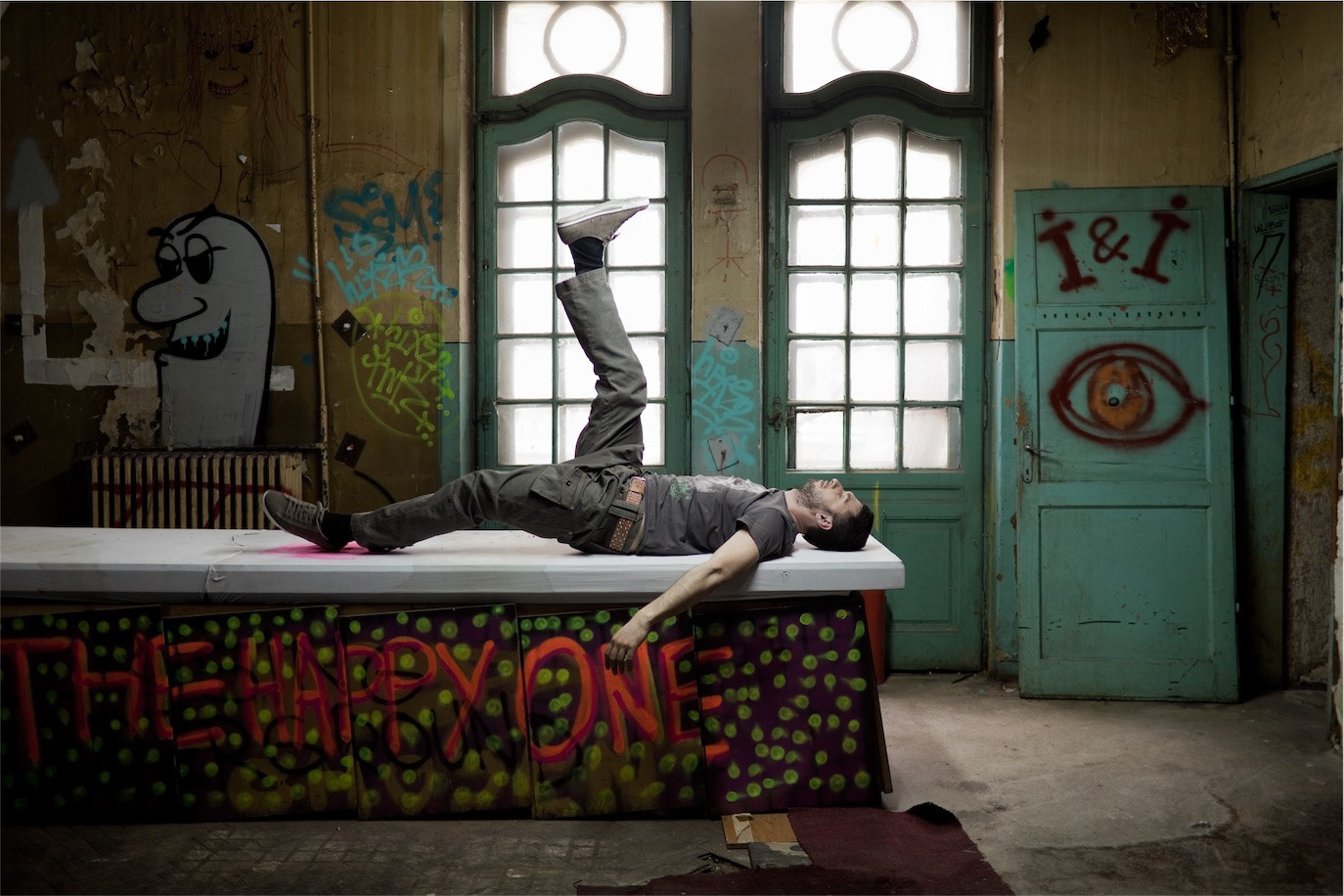 Dragoș Bucur lying on a table in a graffiti-covered abandoned interior, photographed by Alex Gâlmeanu.