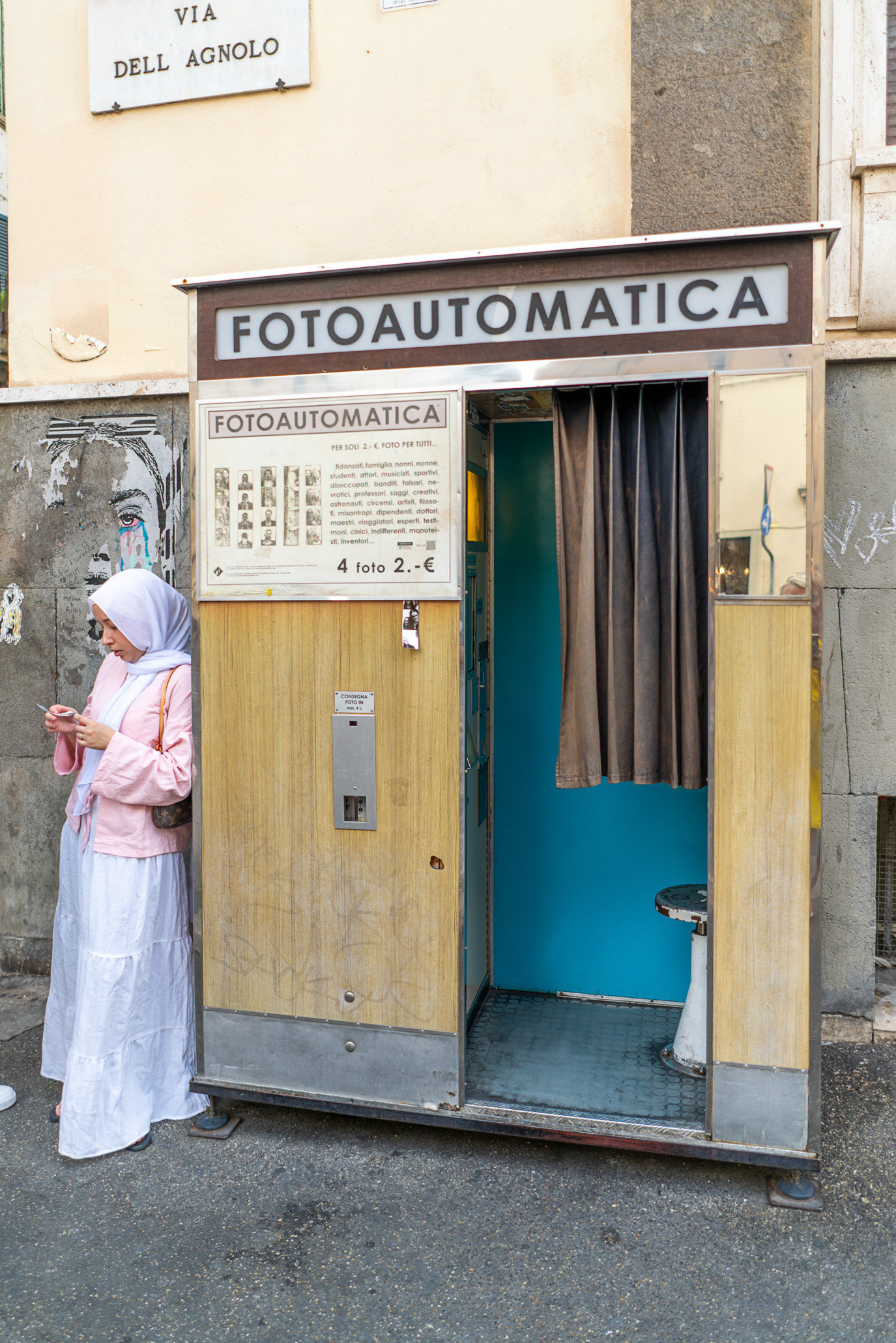 A woman standing beside a vintage Fotoautomatica booth in Florence, Italy. Photograph by Alex Galmeanu.
