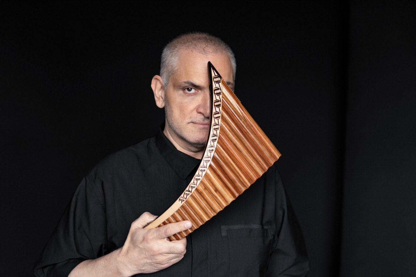 Damian Drăghici holding a pan flute diagonally across one eye, photographed by Alex Gâlmeanu.