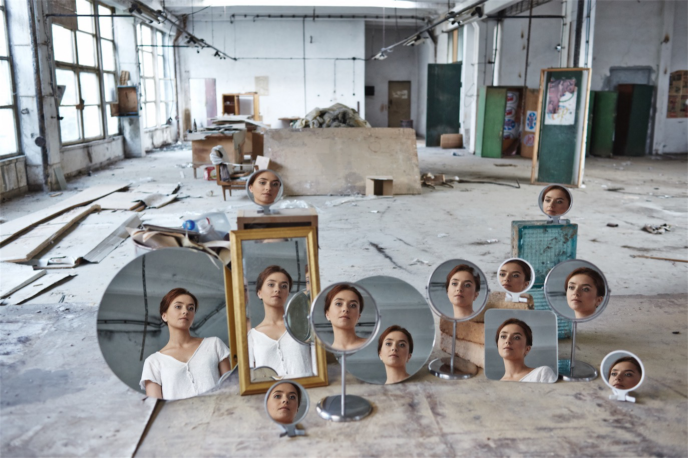 Cosmina Stratan reflected repeatedly in a group of mirrors inside an abandoned industrial space, photographed by Alex Gâlmeanu.