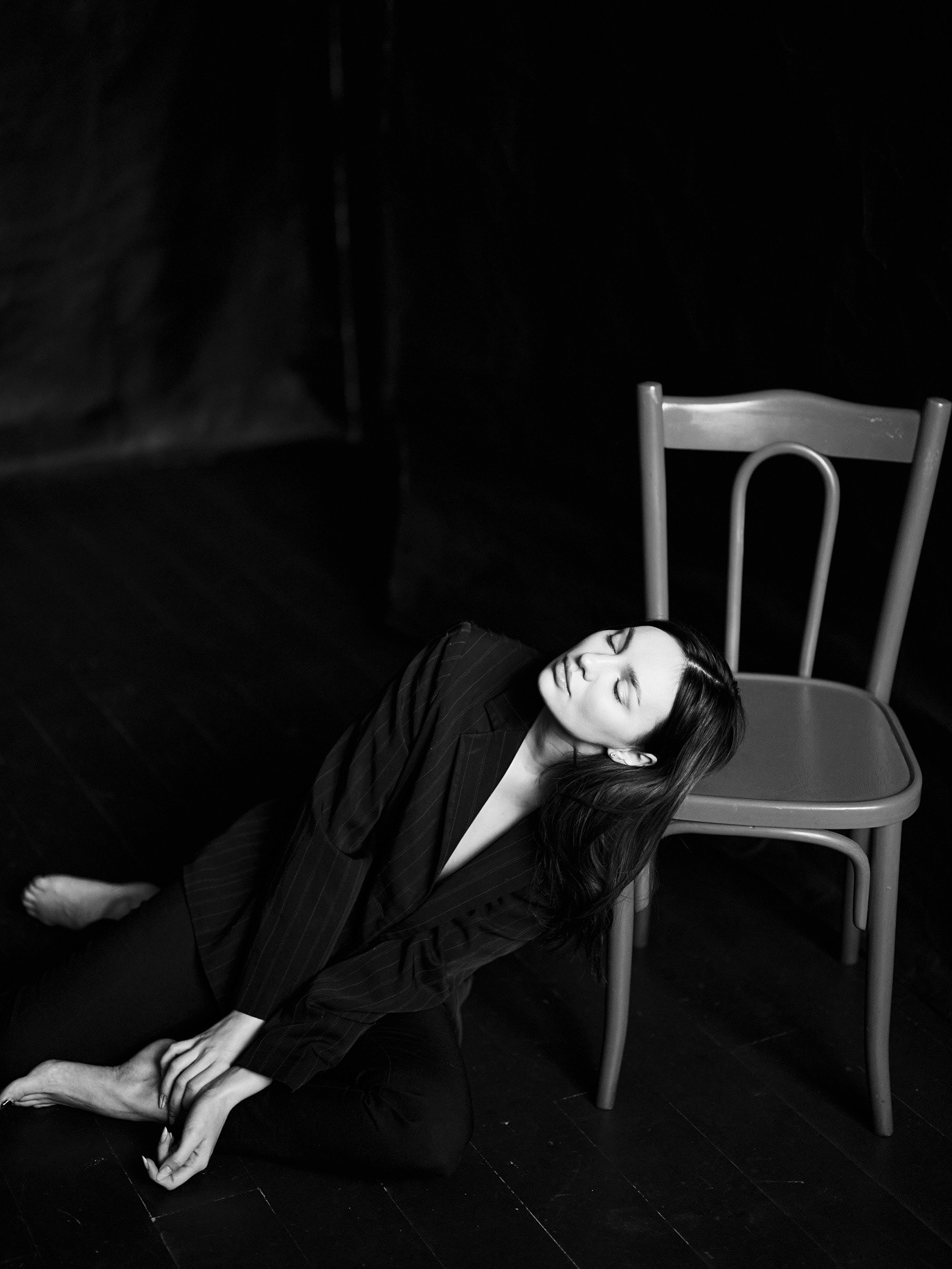 Black-and-white portrait of model Ana Tomouanu reclining on the floor beside a chair, photographed by Alex Gâlmeanu.
