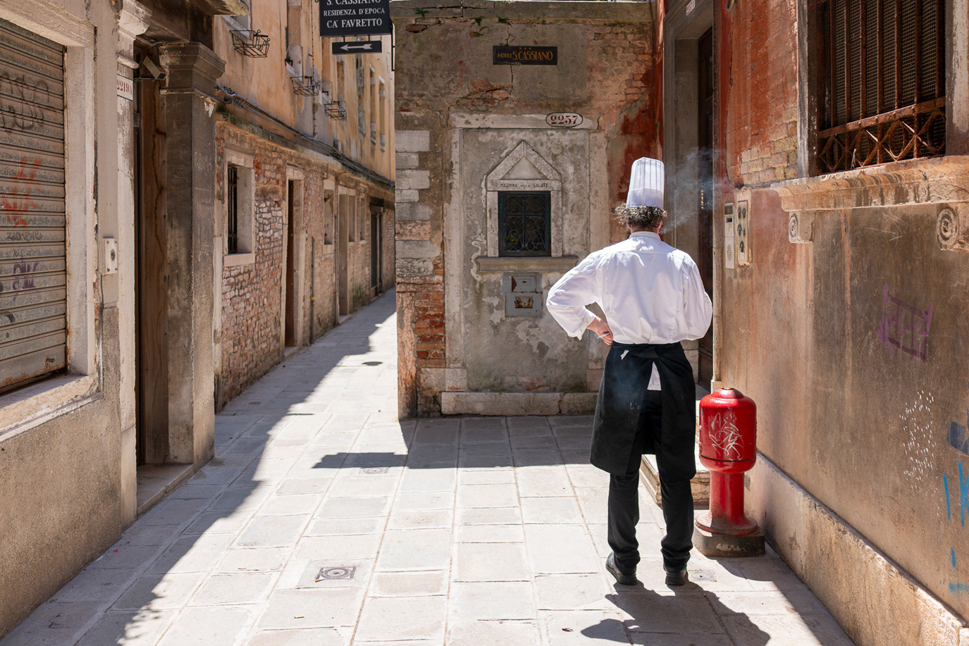 A chef walking through a sunlit alley in Venice, Italy. Photograph by Alex Galmeanu.