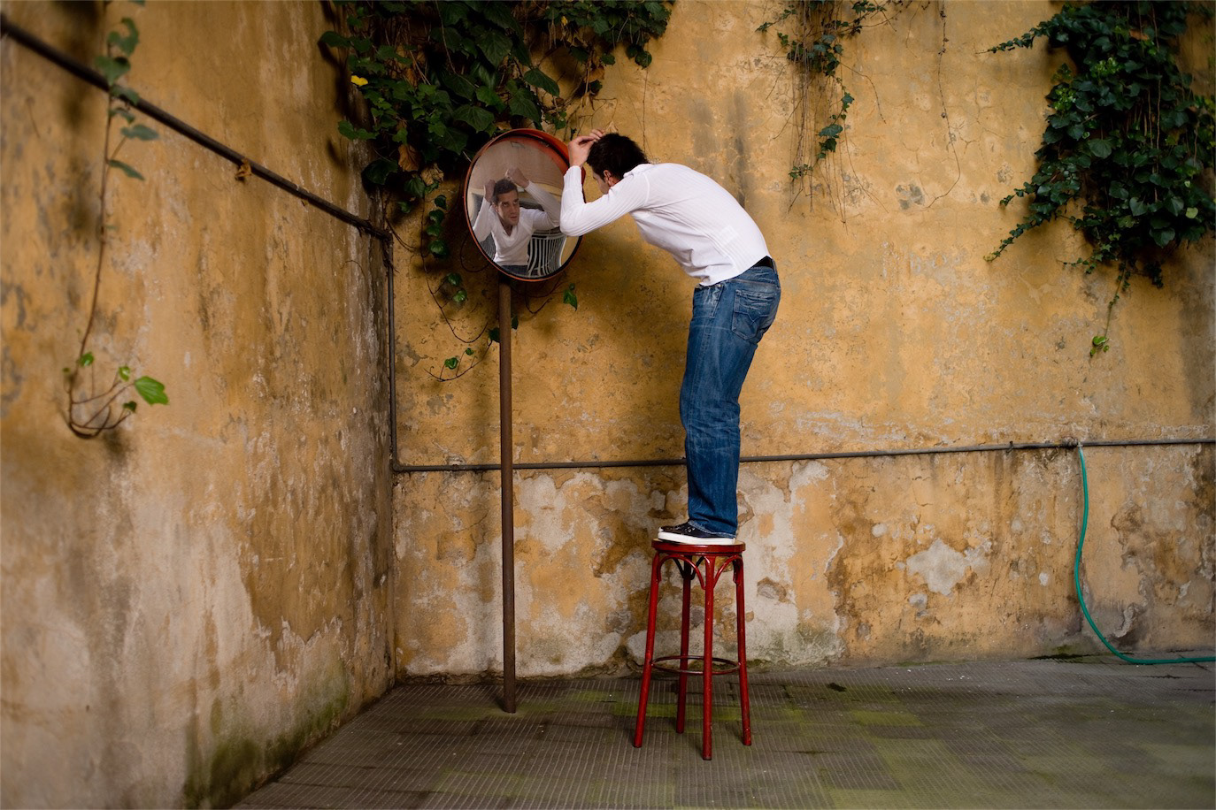 Cristian Chivu standing on a red stool and looking into a wall-mounted mirror, photographed by Alex Gâlmeanu.