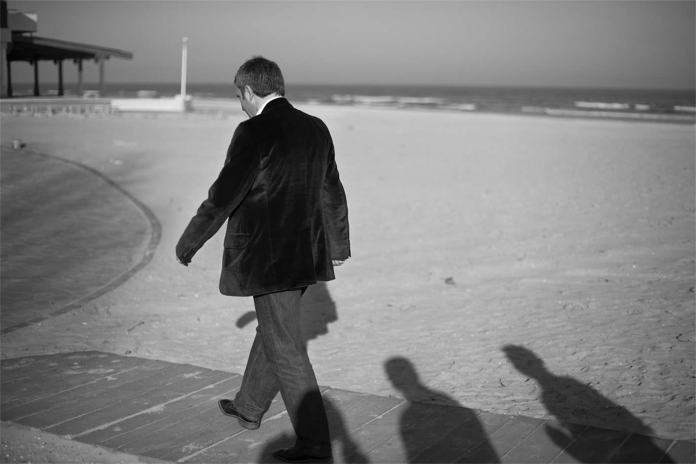 Gheorghe Hagi walking alone along a seaside promenade in black and white, photographed by Alex Gâlmeanu.