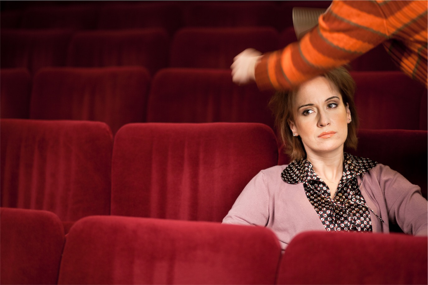 Medeea Marinescu seated among red theatre seats as a stylist reaches into the frame, photographed by Alex Gâlmeanu.