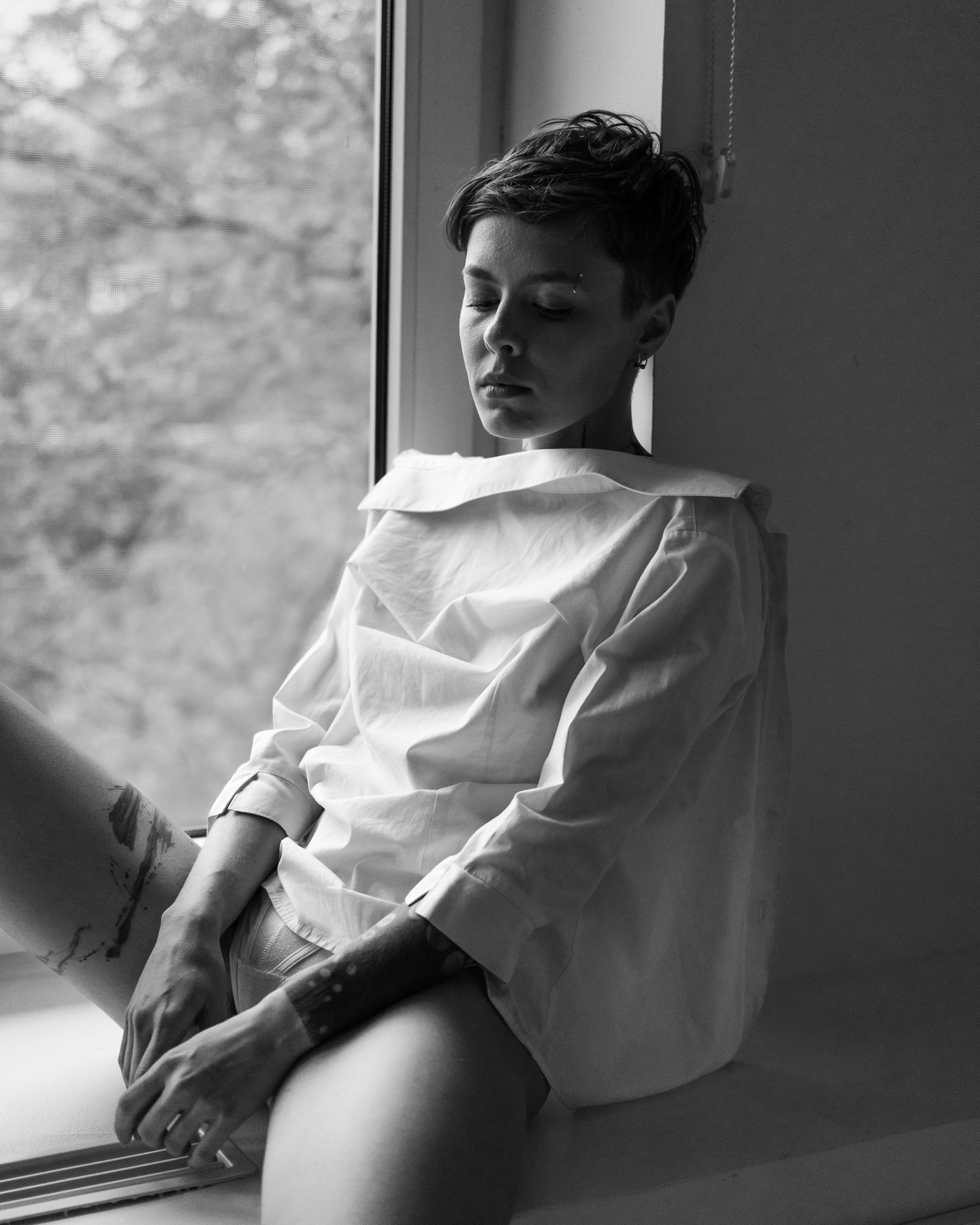 Black-and-white portrait of model Irina Ludosanu seated by a window in a white shirt, photographed by Alex Gâlmeanu.