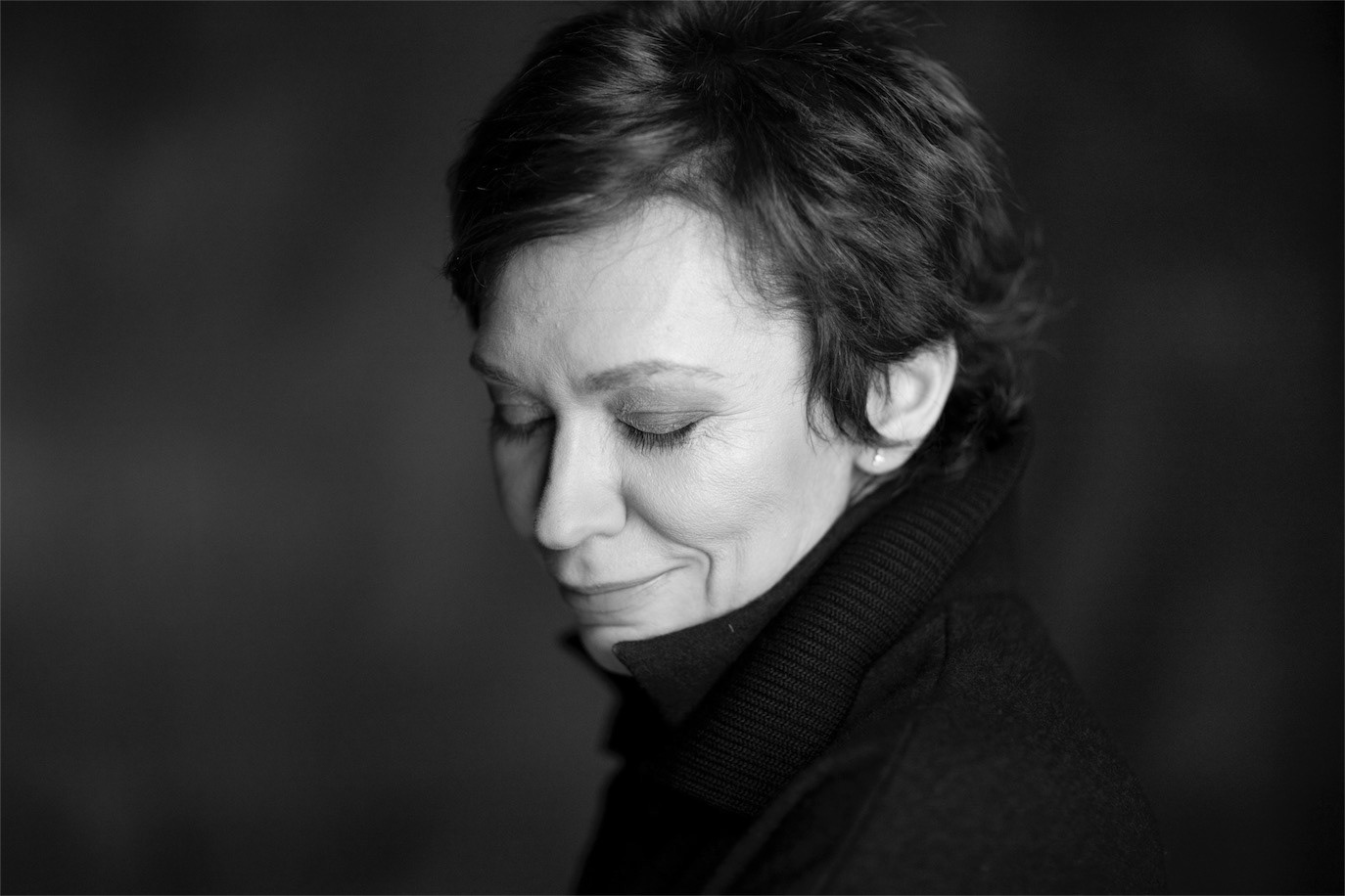 Black-and-white close-up of Oana Pellea with her eyes lowered and a subtle smile, photographed by Alex Gâlmeanu.