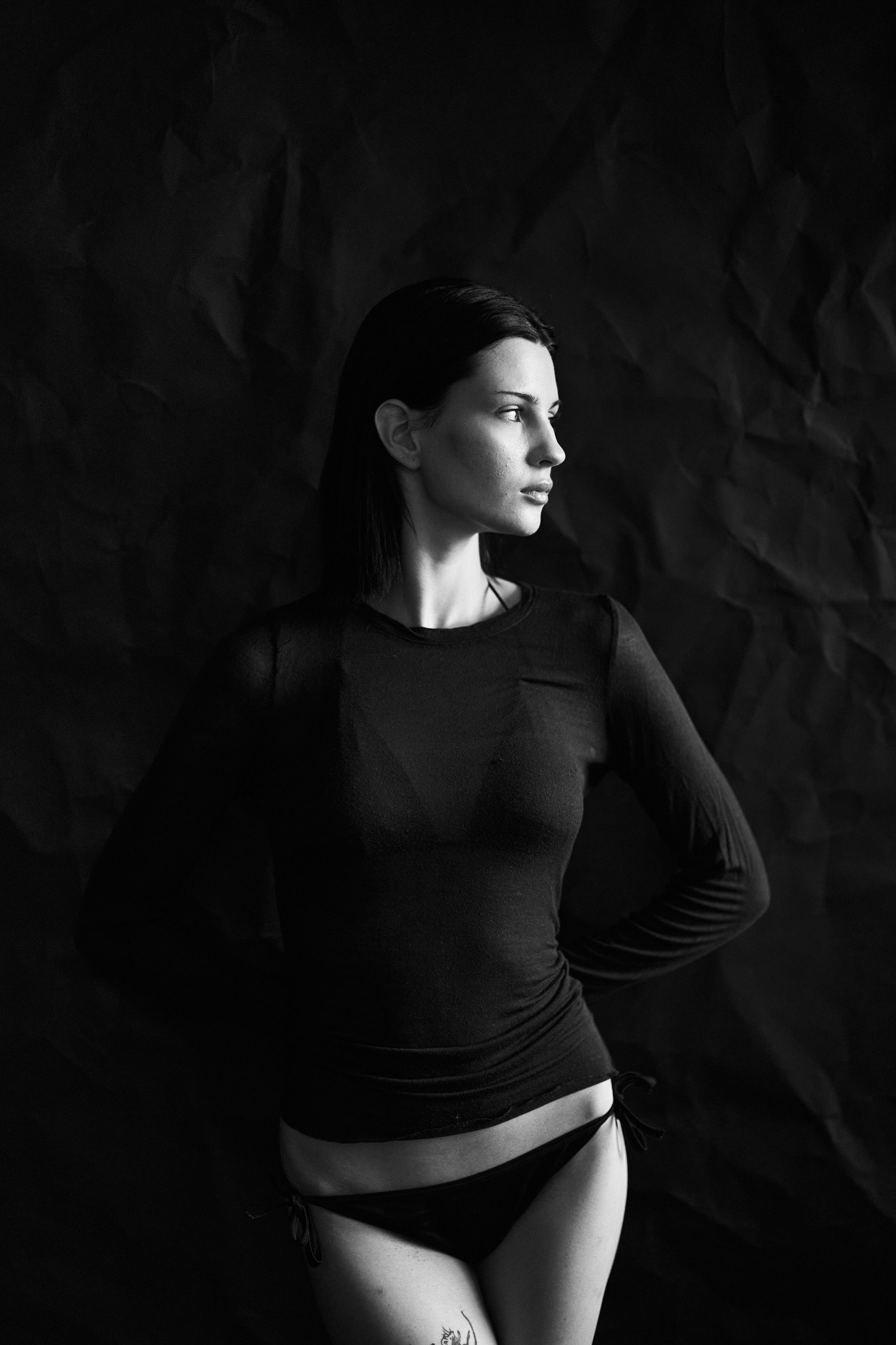 Black-and-white full-length portrait of model Alexia Tomeci standing in hard studio light, photographed by Alex Gâlmeanu.