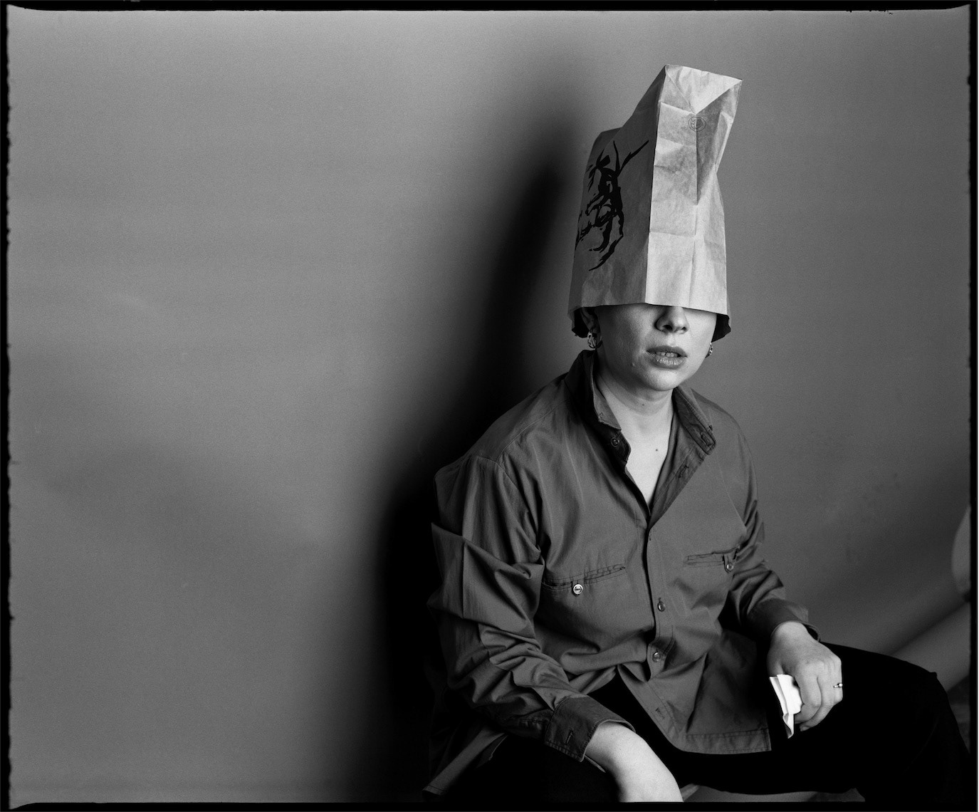Teo Trandafir seated with a paper bag covering her head in a black-and-white portrait, photographed by Alex Gâlmeanu.
