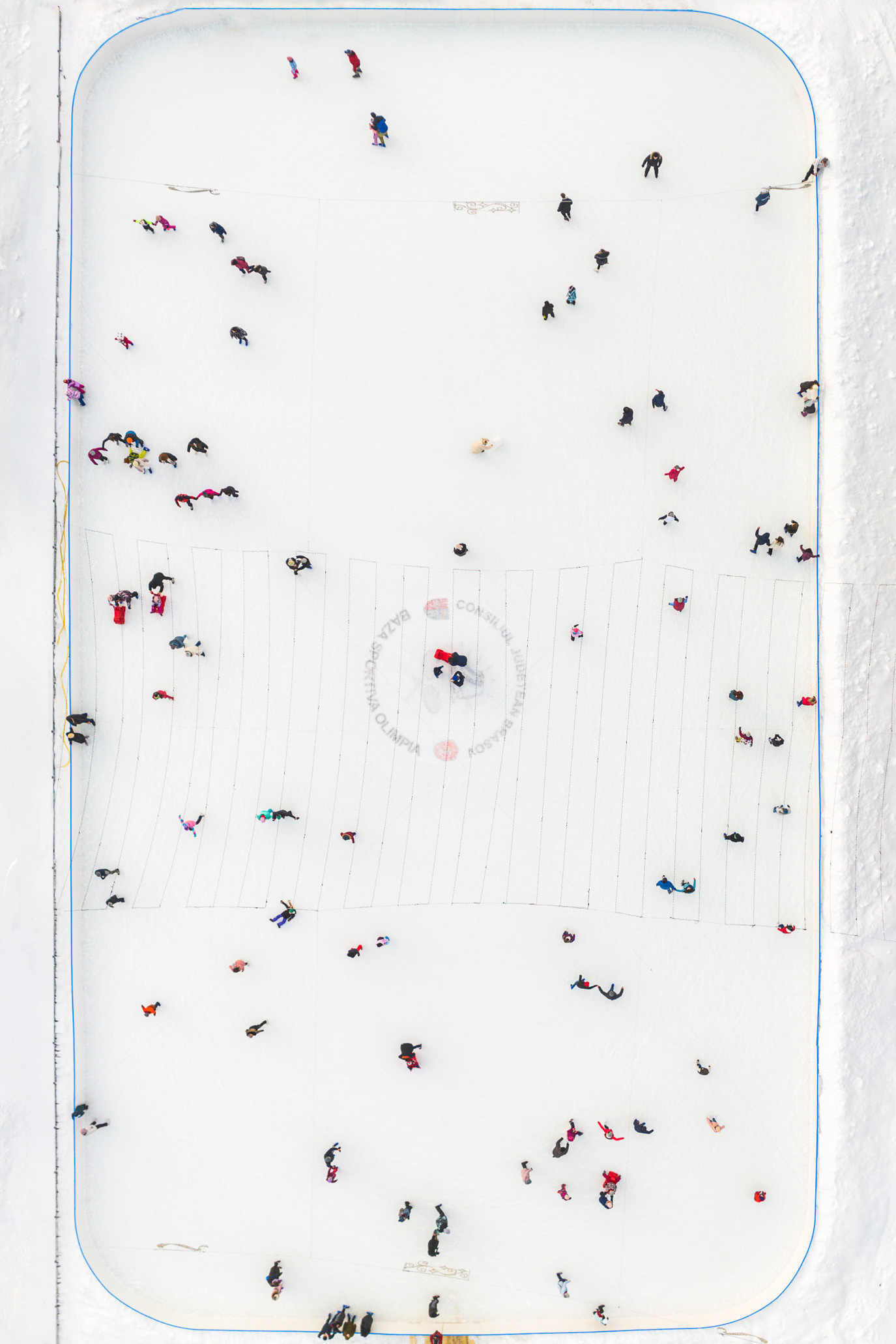 Skaters scattered across a white ice rink seen from above in Brașov, Romania. Photograph by Alex Galmeanu.