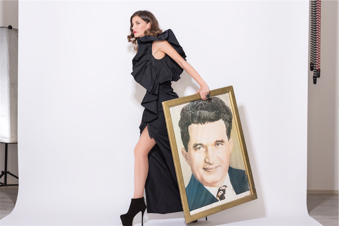 Diana Dondoe in a sculptural black dress holding a large framed portrait, photographed by Alex Gâlmeanu.