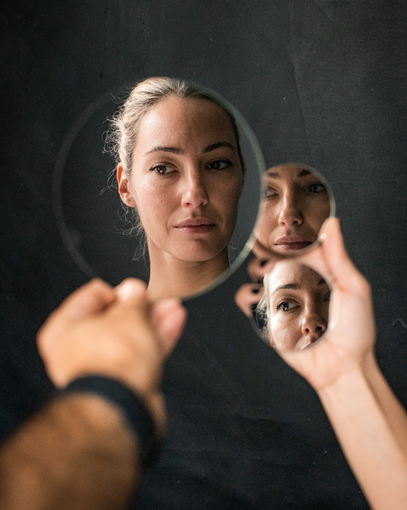Portrait of actor Raluca Aprodu holding small mirrors that fragment her reflection, photographed by Alex Gâlmeanu.