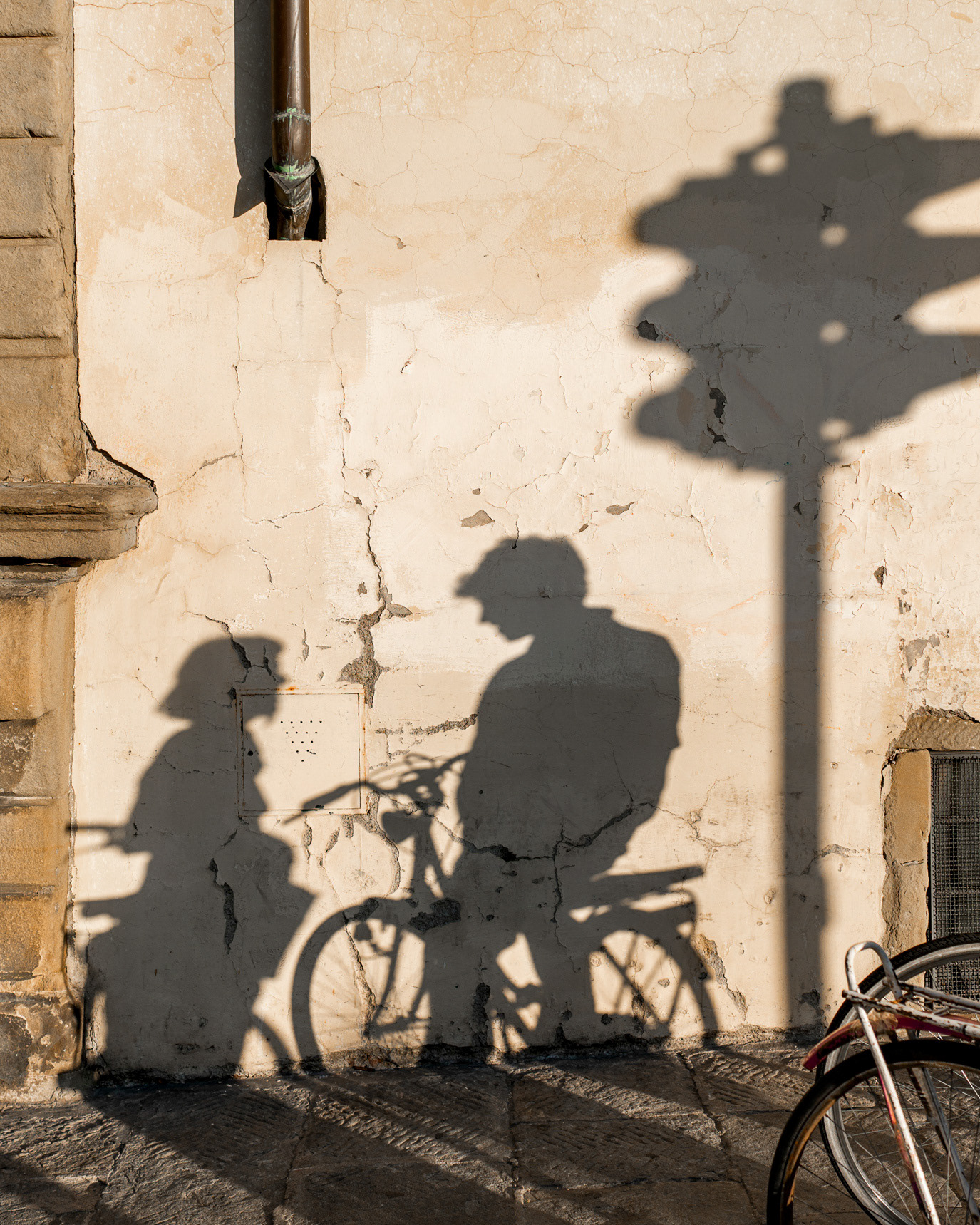 Shadows of two people and a bicycle on a stone wall in Florence, Italy. Photograph by Alex Gâlmeanu.