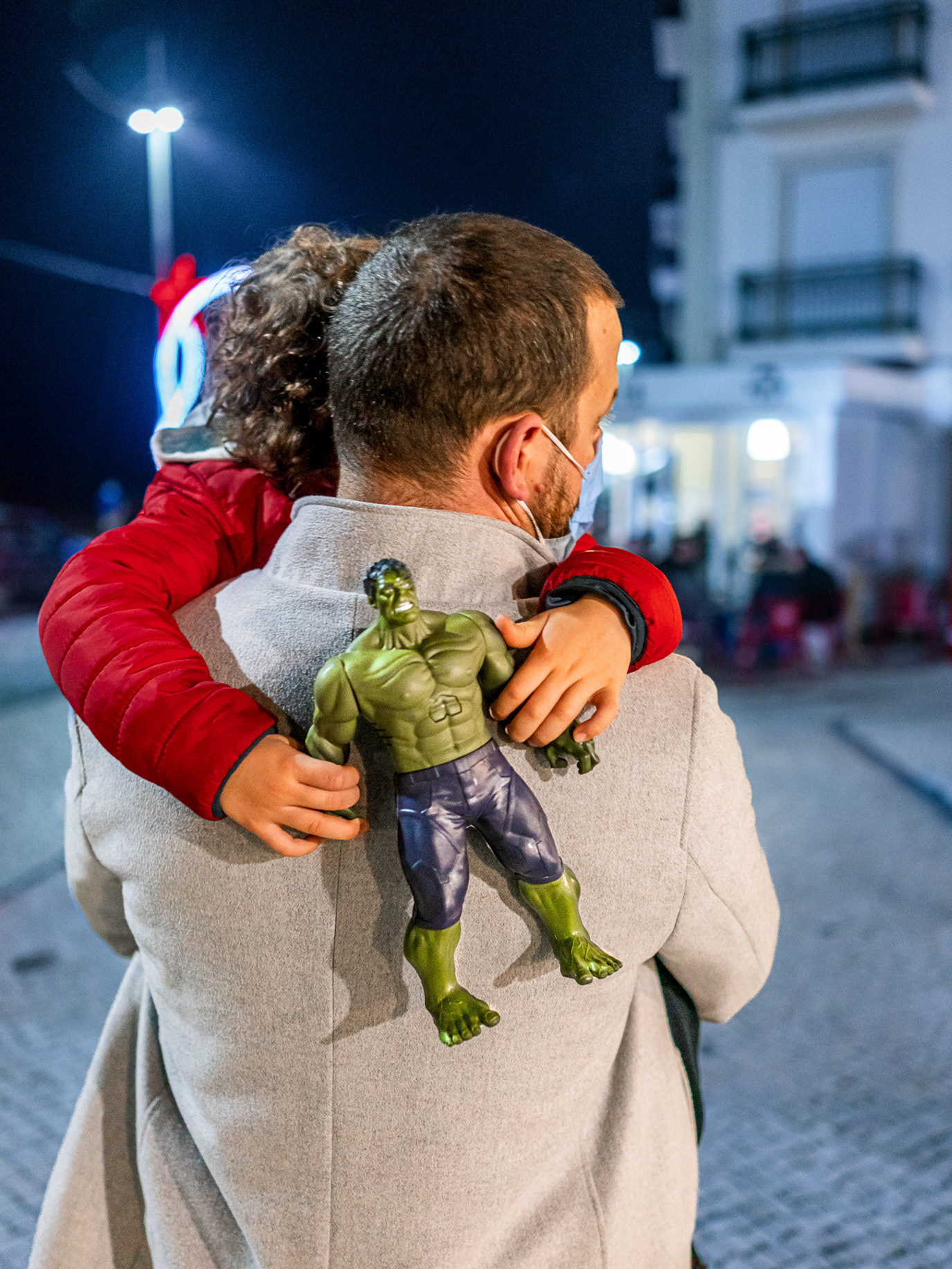 A father carrying a child holding a Hulk toy in Ericeira, Portugal. Photograph by Alex Galmeanu.