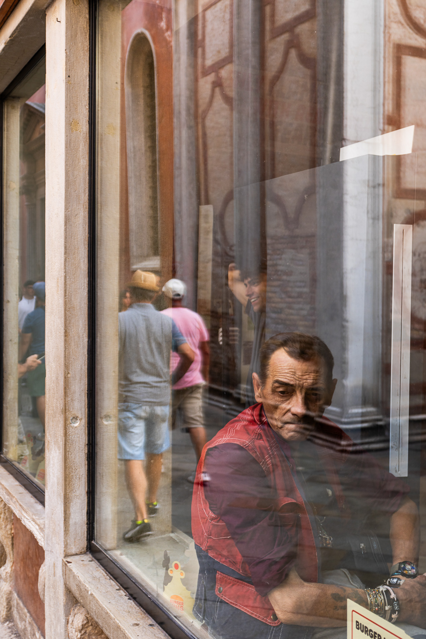 A seated man layered with street reflections in a window in Venice, Italy. Photograph by Alex Galmeanu.