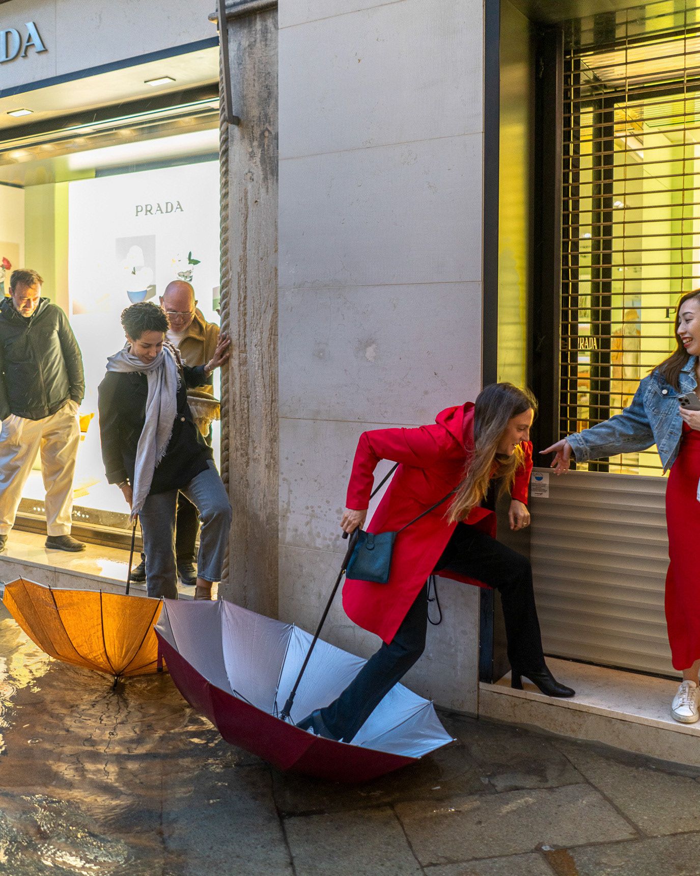 Women gathered around a collapsed red umbrella on a wet street in Venice, Italy. Photograph by Alex Galmeanu.