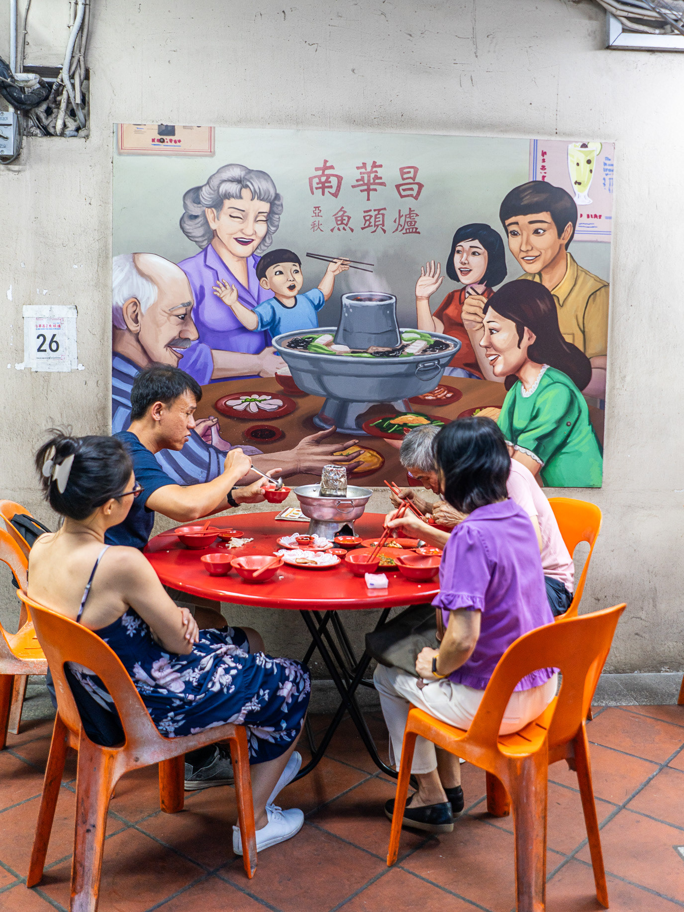 Diners seated beneath a painted family feast in Singapore. Photograph by Alex Gâlmeanu.