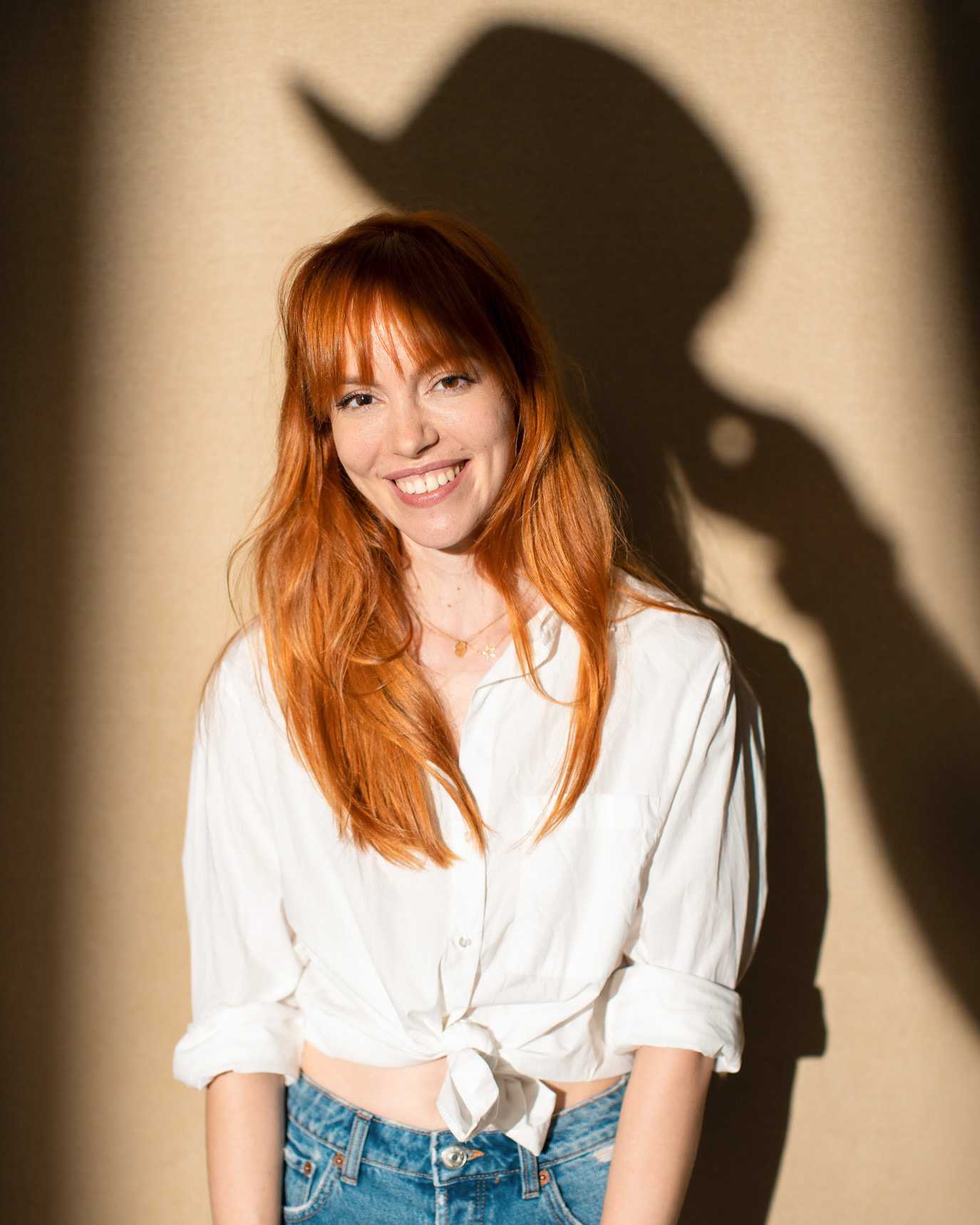 Portrait of actor Olimpia Melinte smiling in a white shirt with her shadow on the wall, photographed by Alex Gâlmeanu.