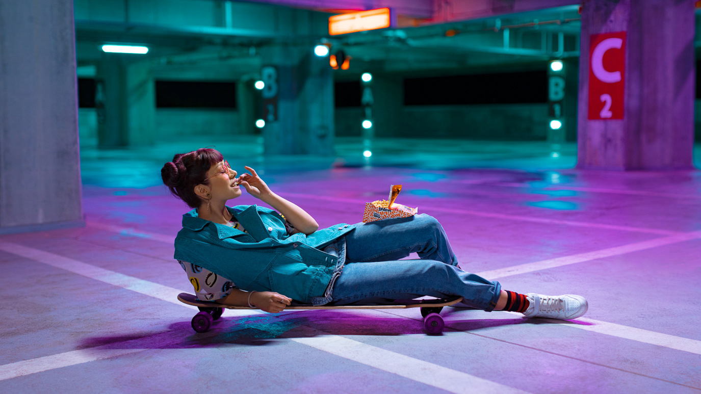 Woman reclining on a skateboard in a neon-lit parking garage for Alka, photographed by Alex Gâlmeanu.
