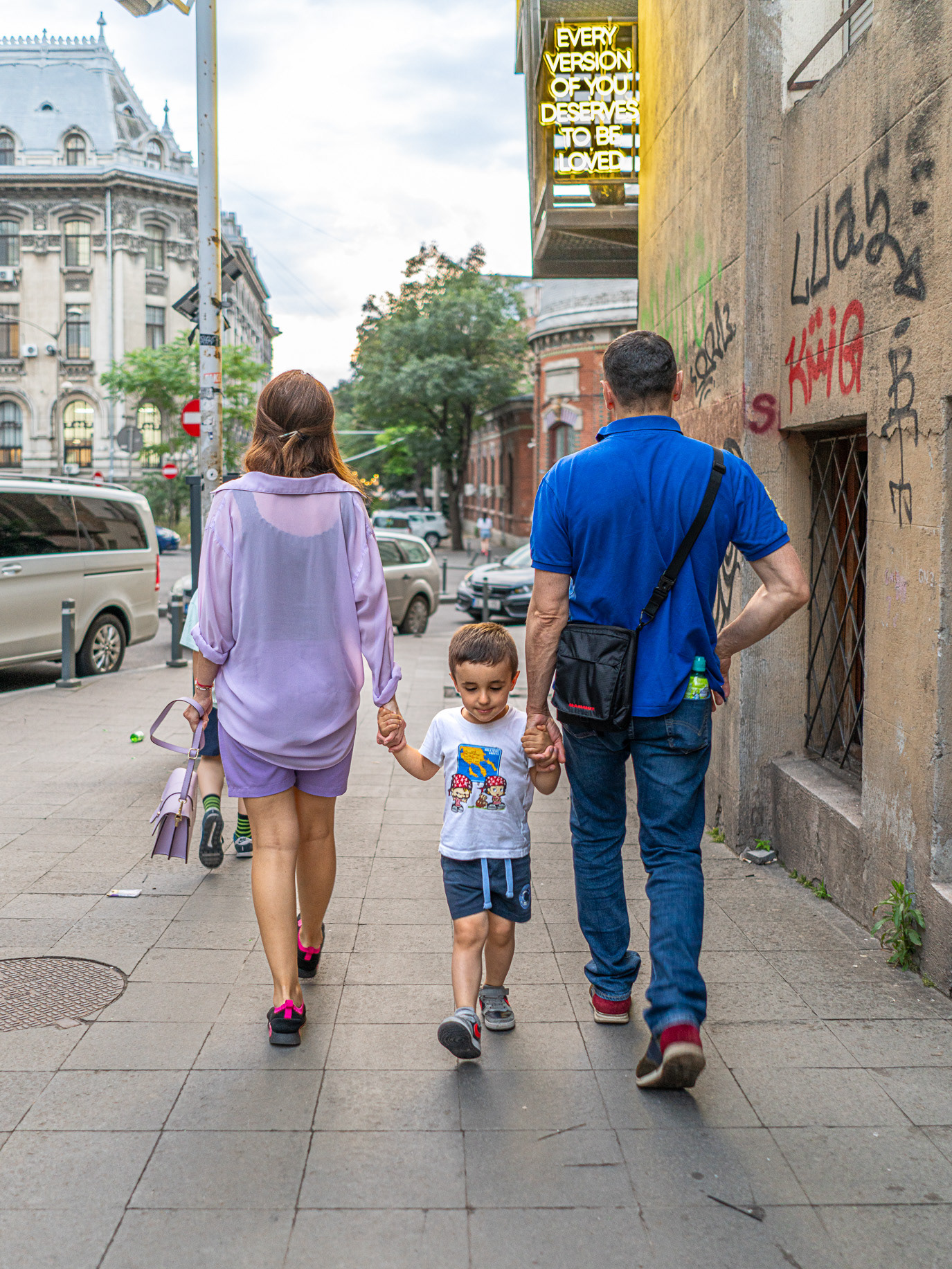 A family holding hands beneath a neon message about love in Bucharest, Romania. Photograph by Alex Galmeanu.