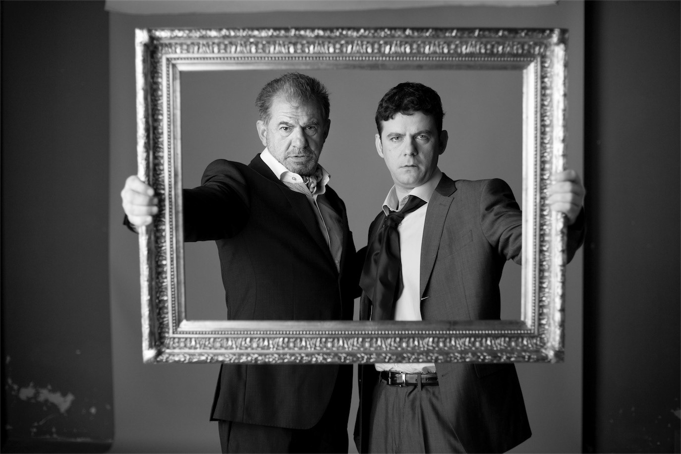 Florin Zamfirescu and Răzvan Zamfirescu standing within an ornate empty frame, photographed by Alex Gâlmeanu.