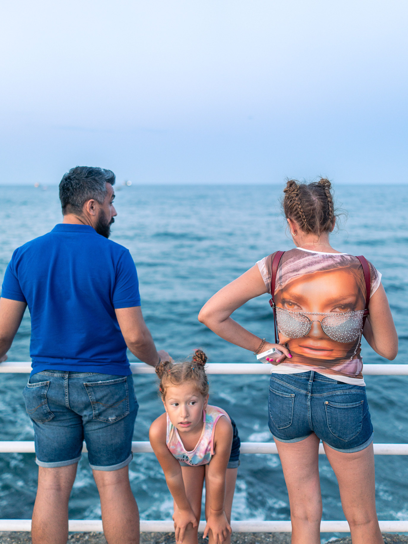 A child bending forward between her parents on the seafront in Constanța, Romania. Photograph by Alex Galmeanu.