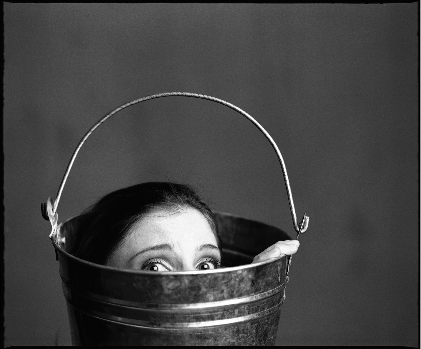 Mihaela Călinoiu peeking from inside a metal bucket in a black-and-white portrait, photographed by Alex Gâlmeanu.