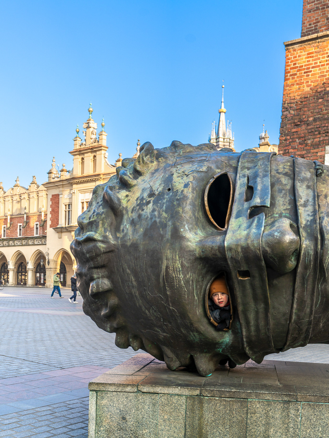 A child peering through the opening of a monumental bronze head in Kraków, Poland. Photograph by Alex Galmeanu.