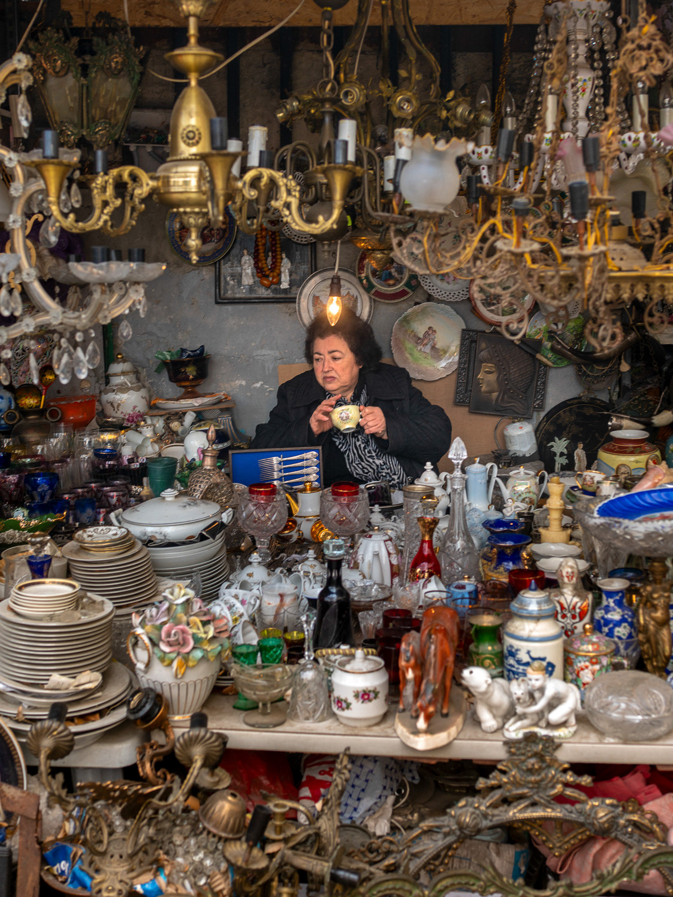 A woman seated inside a densely packed antique shop in Tbilisi, Georgia. Photograph by Alex Galmeanu.