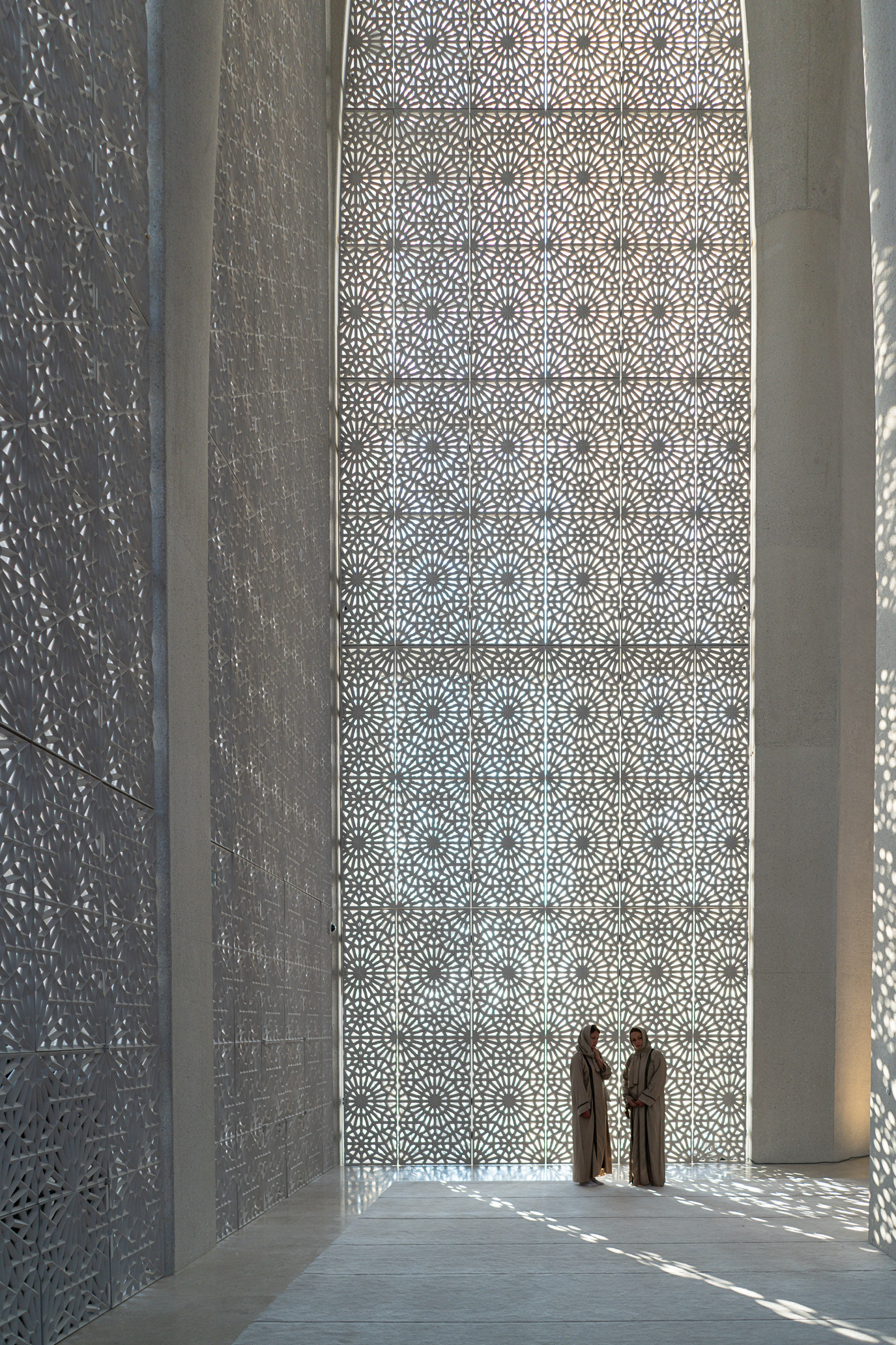 Two small figures standing beneath a monumental patterned arch in Abu Dhabi, UAE. Photograph by Alex Galmeanu.