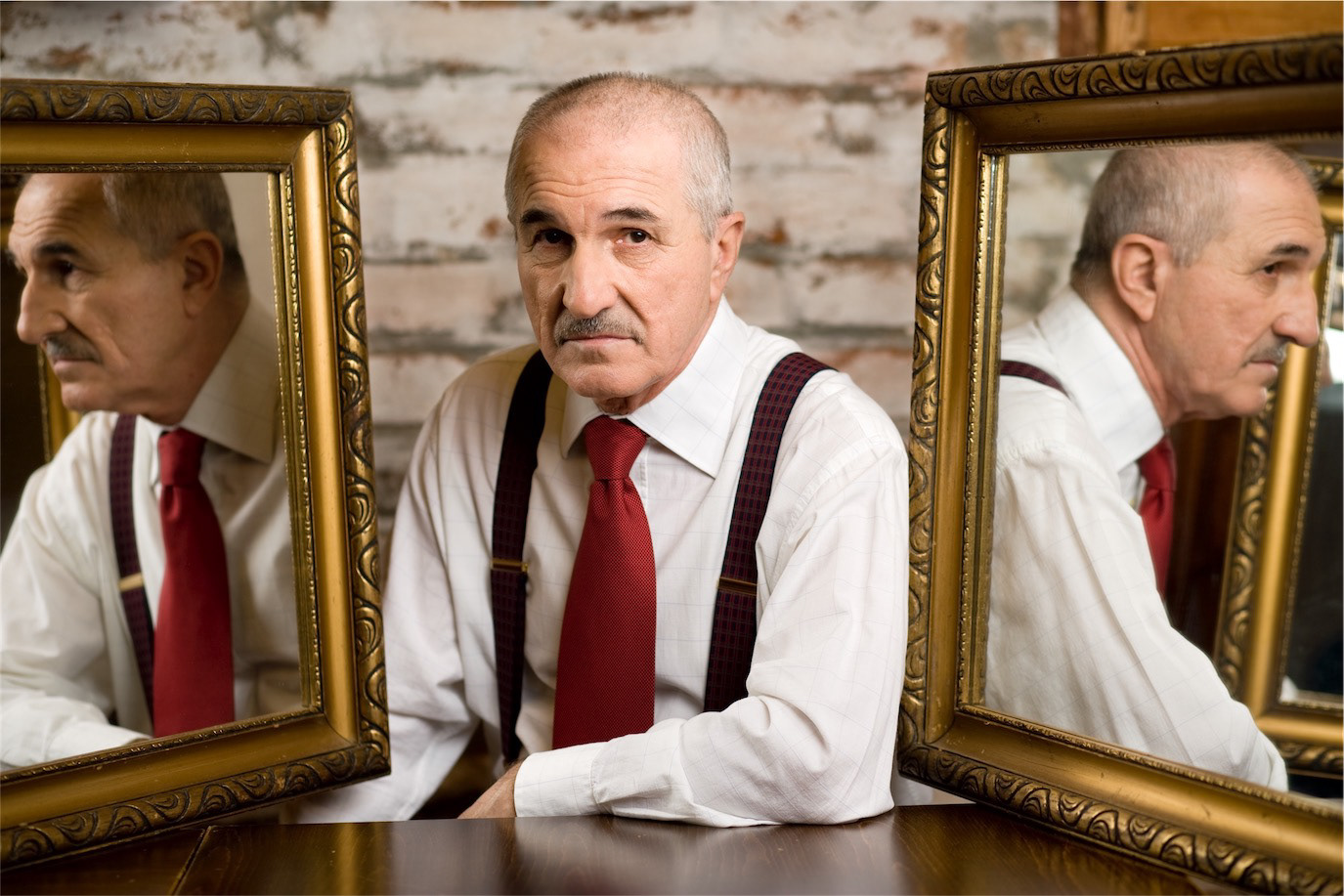 Gheorghe Dinică seated between two framed mirrors reflecting his profile, photographed by Alex Gâlmeanu.