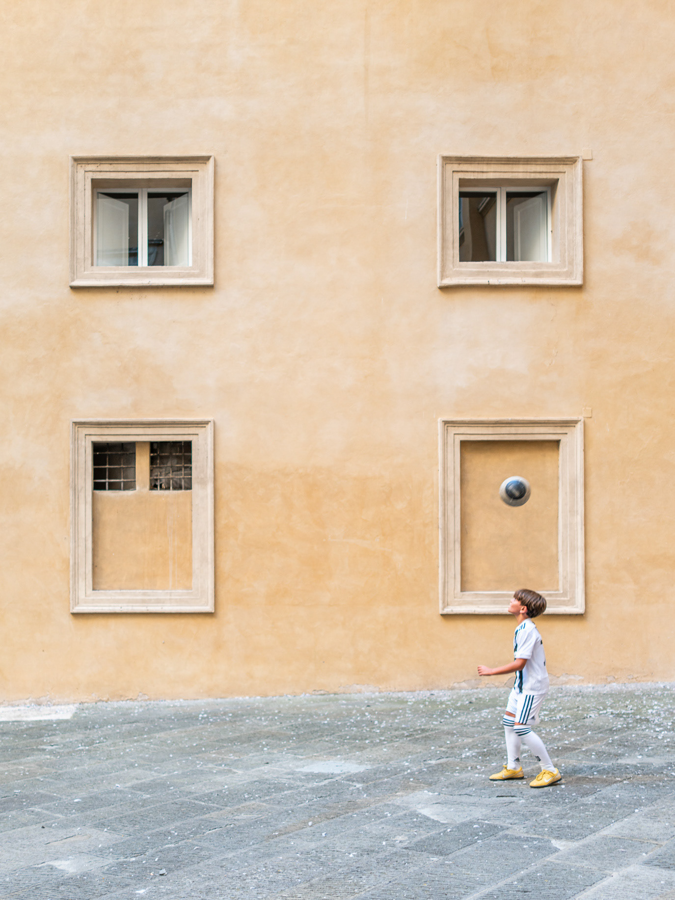A child walking beneath four square windows in Siena, Italy. Photograph by Alex Galmeanu.