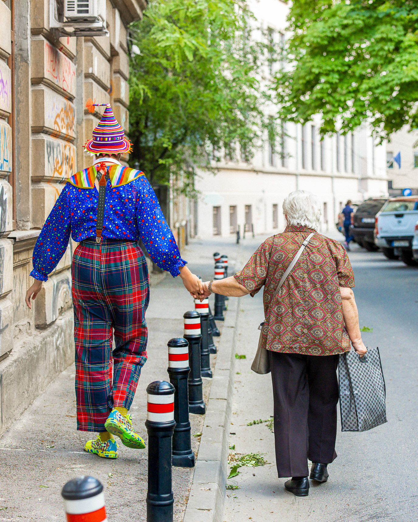 A clown-like person walking hand in hand with an elderly woman in Bucharest, Romania. Photograph by Alex Galmeanu.
