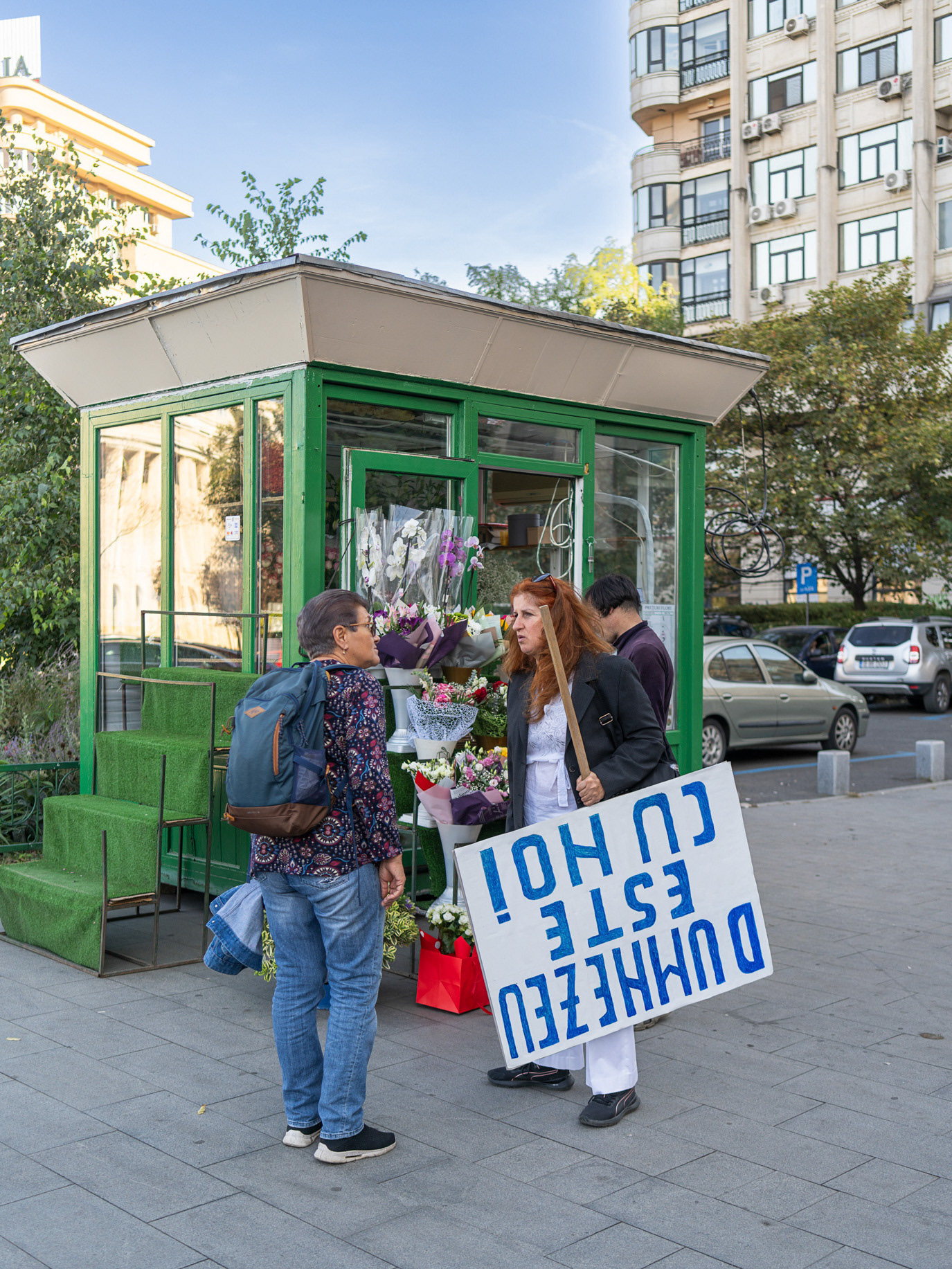 A couple holding an upside-down sign outside a flower kiosk in Bucharest, Romania. Photograph by Alex Galmeanu.