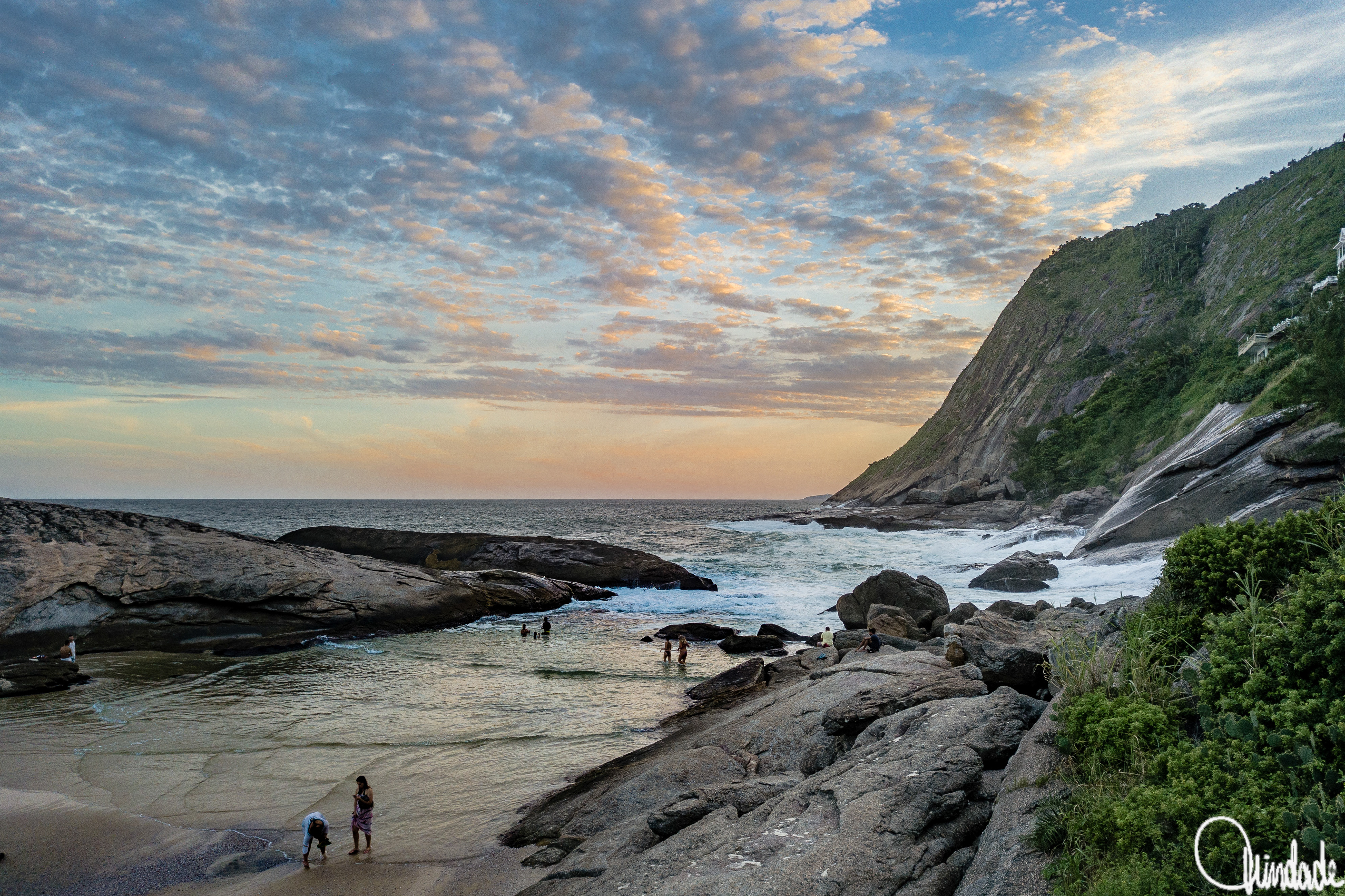 Costa rochosa de Itacoatiara, Niterói (RJ), iluminada pelo pôr do sol com pessoas na areia.