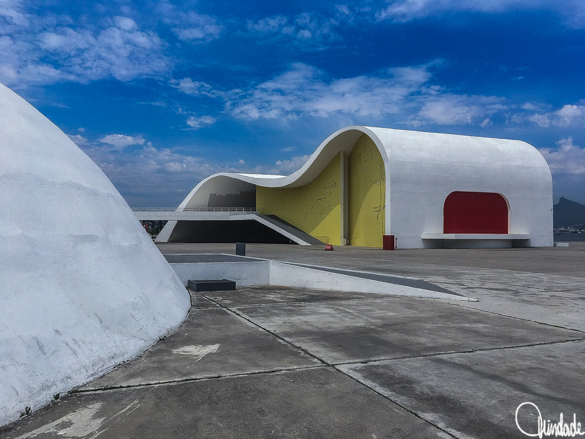 Edifício moderno com linhas curvas e fachada branca, painel amarelo e abertura vermelha. Cobertura ondulada lembra ondas do mar. Estrutura faz parte do Caminho Niemeyer, em Niterói, RJ.