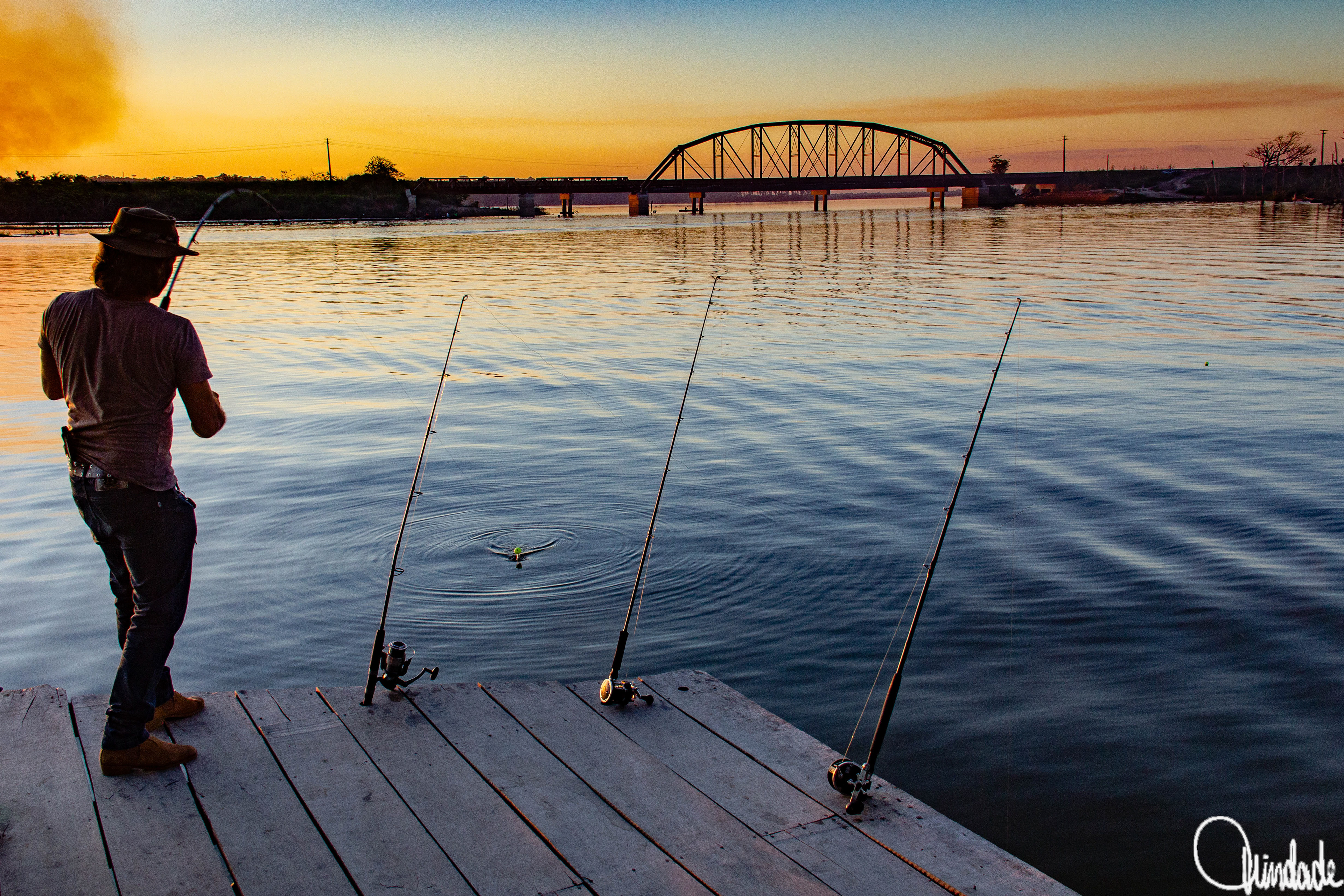 Pescador no rio Jaci Paraná, em Porto Velho (RO), durante o pôr do sol, com a ponte metálica da ferrovia Madeira-Mamoré ao fundo.