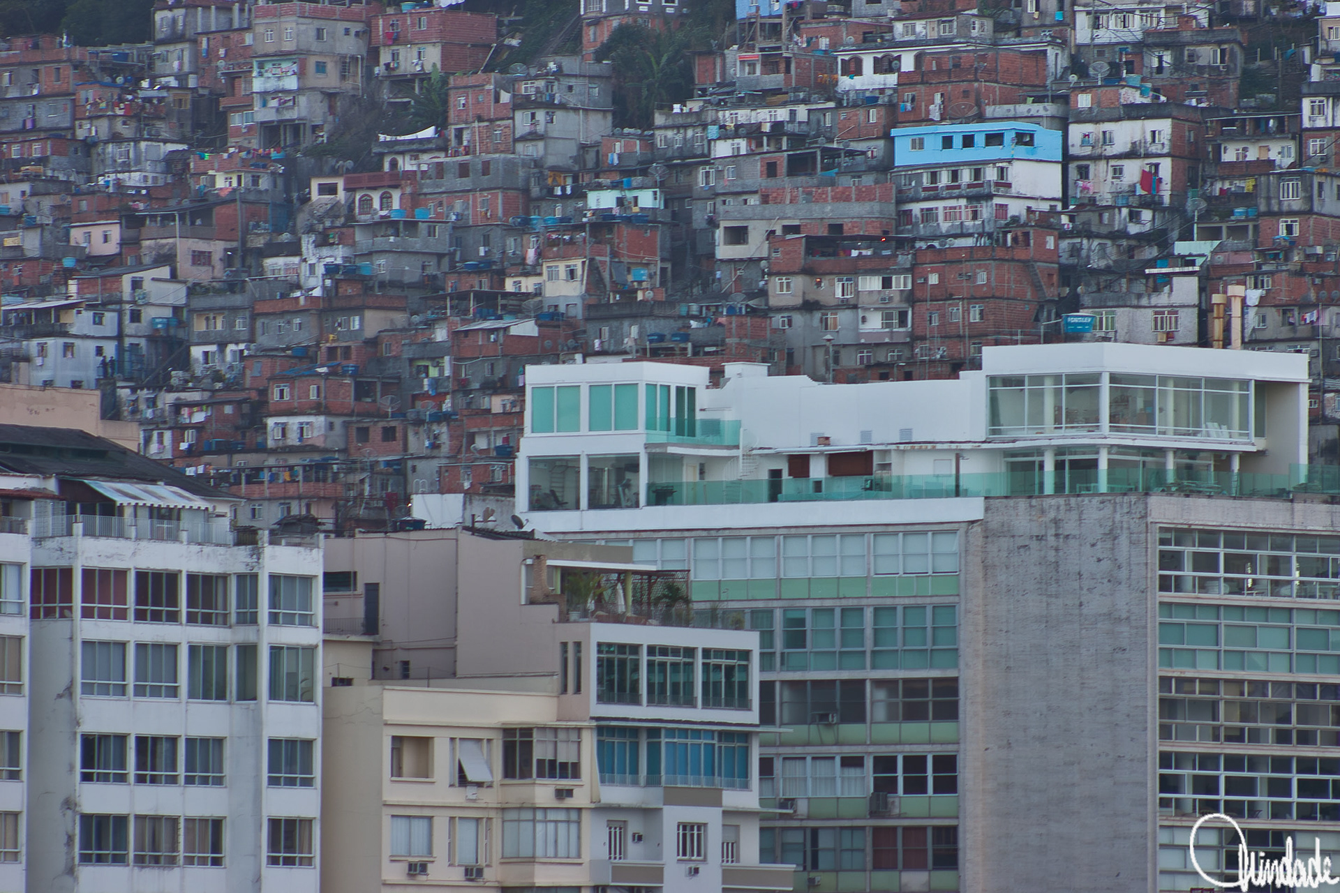 Cena urbana em Copacabana, Rio de Janeiro, mostrando edifícios residenciais contemporâneos com fachadas envidraçadas em primeiro plano e, ao fundo, uma favela densamente construída na encosta. A imagem destaca o contraste arquitetônico e social entre moradias formais e informais.