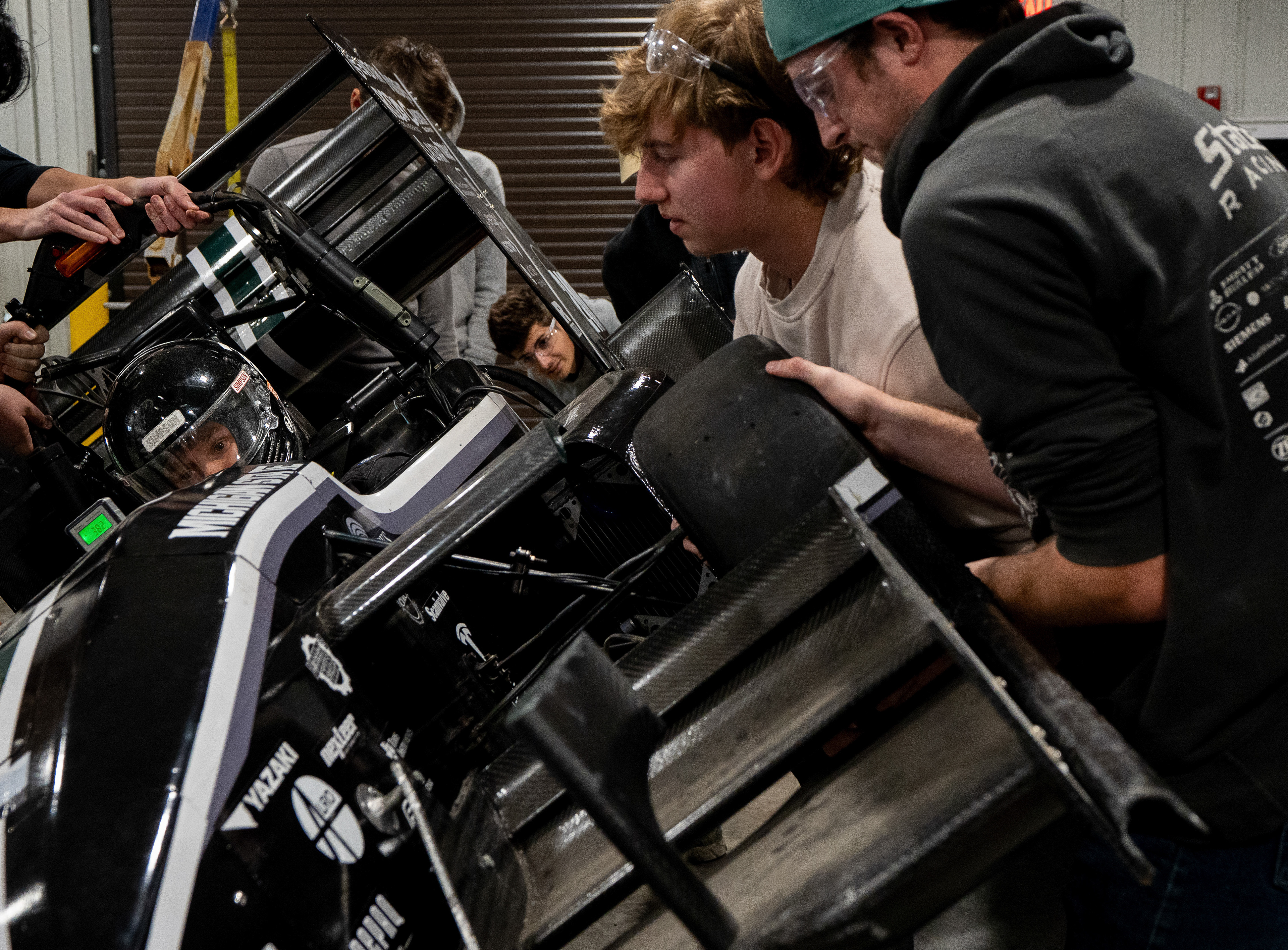 Member of MSU Formula Club, Carter Ross, sits in the MSU Formula SAE car during a center of gravity test at Michigan State University's William A. Demmer Engineeing Center in East Lansing, Michigan, on Saturday, Nov. 8, 2025. The car is lifted until equilibrium which is about 45 degrees off the ground.