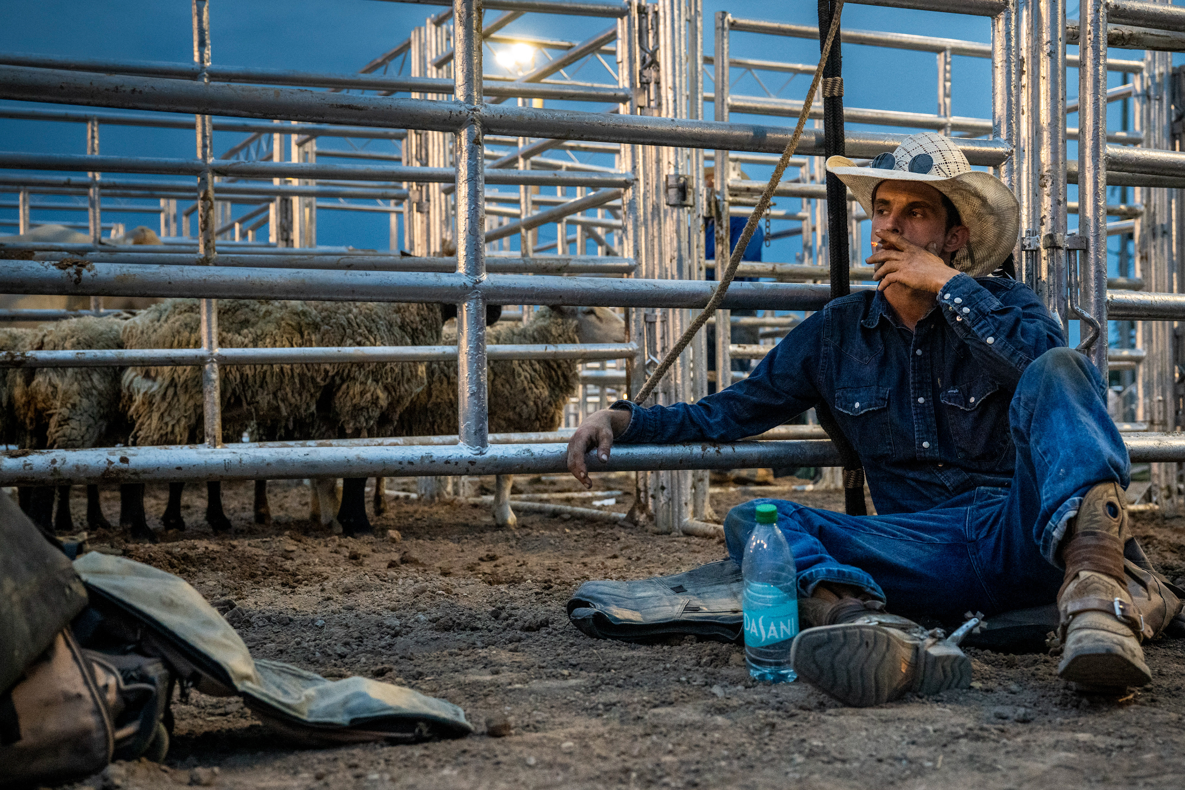 Sam Gravling, 29, smokes a cigarette while sitting in the dirt beside the livestock pens during the Super Kicker Rodeo on Aug. 18, 2026, in Midland, Mich.