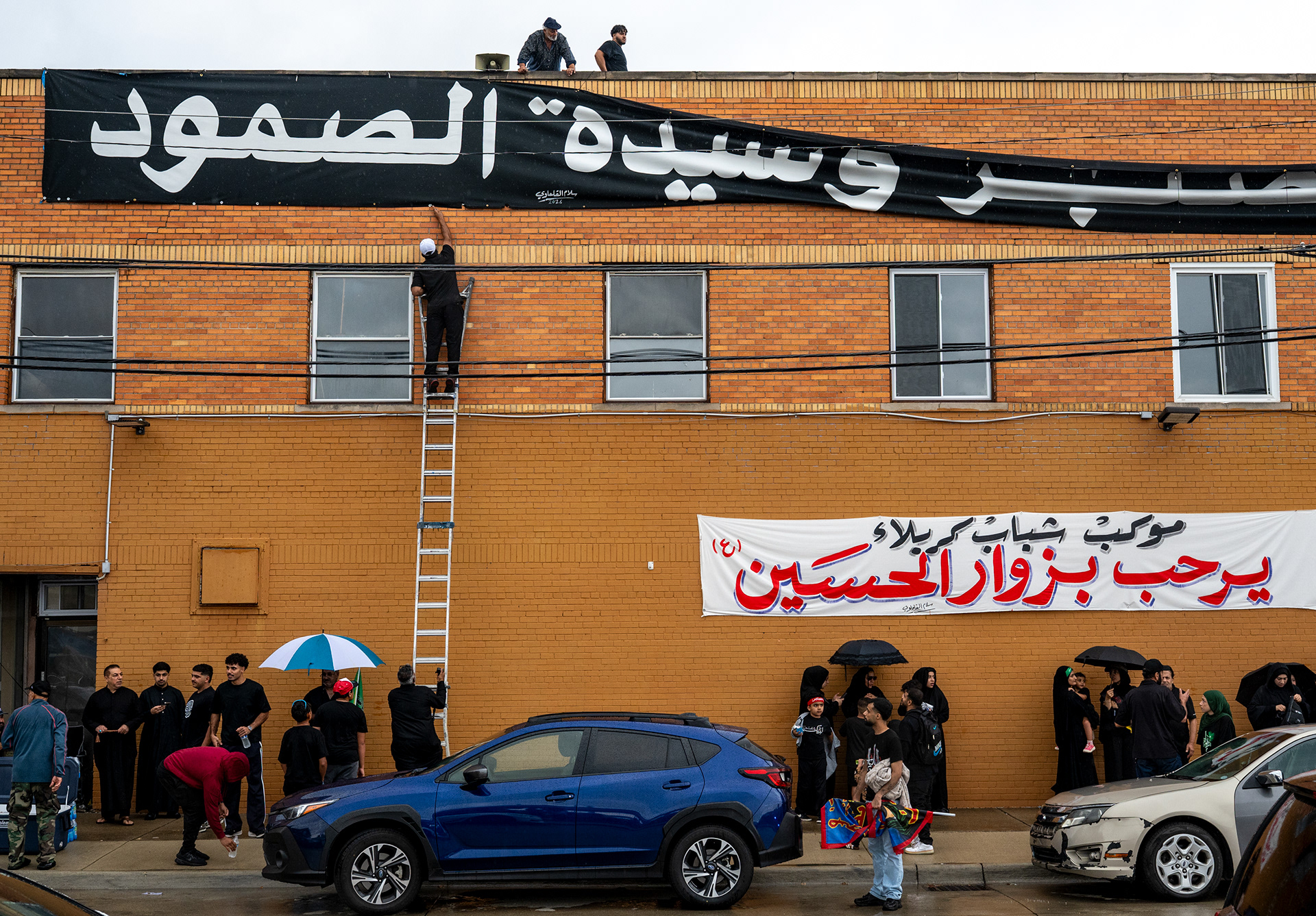 Ali Almagibi, 38, climbs a latter to take down a sign to walk with before thousands walk during the Arbaeen procession Sunday, Aug. 2, 2026, in Dearborn, Mich. The annual procession marks the end of the 40 days of mourning in the Shi'a tradition honoring the death of Imam Husayn, the grandson of the Prophet Muhammad, at the Battle of Karbala in 680.