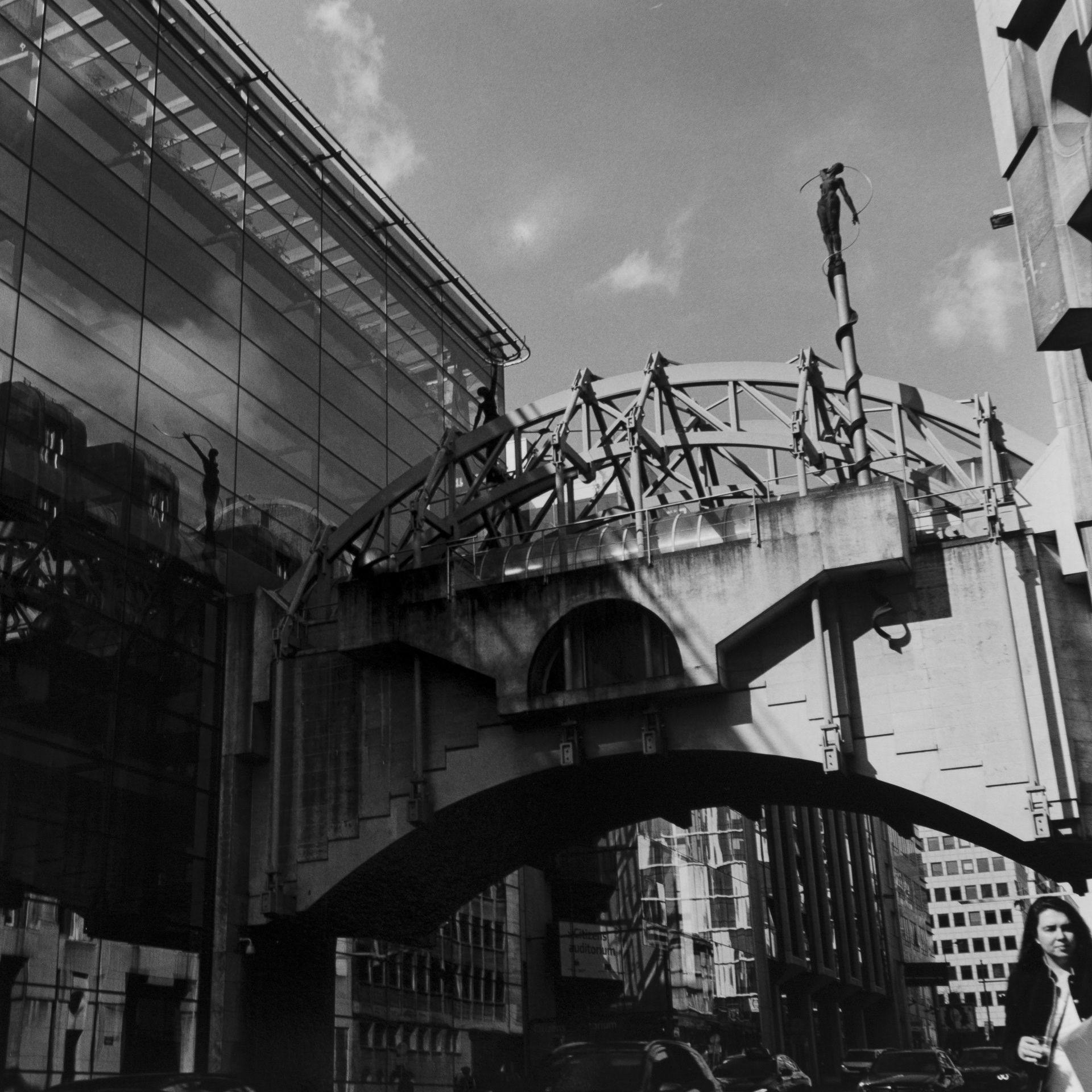 Passerella su Rue Belliard (all’altezza del civico 97) studio di architettura Group Planning – 1983. La passerella è sormanotata da due statue in posizione simmetrica che rappresentano Arianna ed il suo filo d’oro per trarre Teseo dal labirinto, opera di Jean-Paul Laenen - 1991