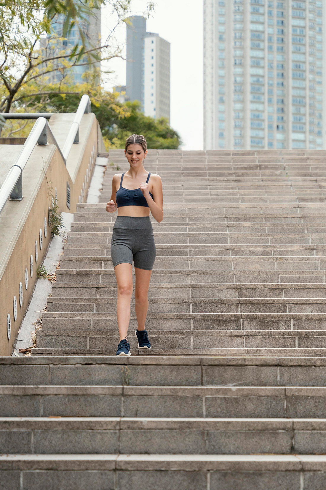 Add woman in sports bra and grey shorts jogging down wide outdoor stone stairs in a city park.